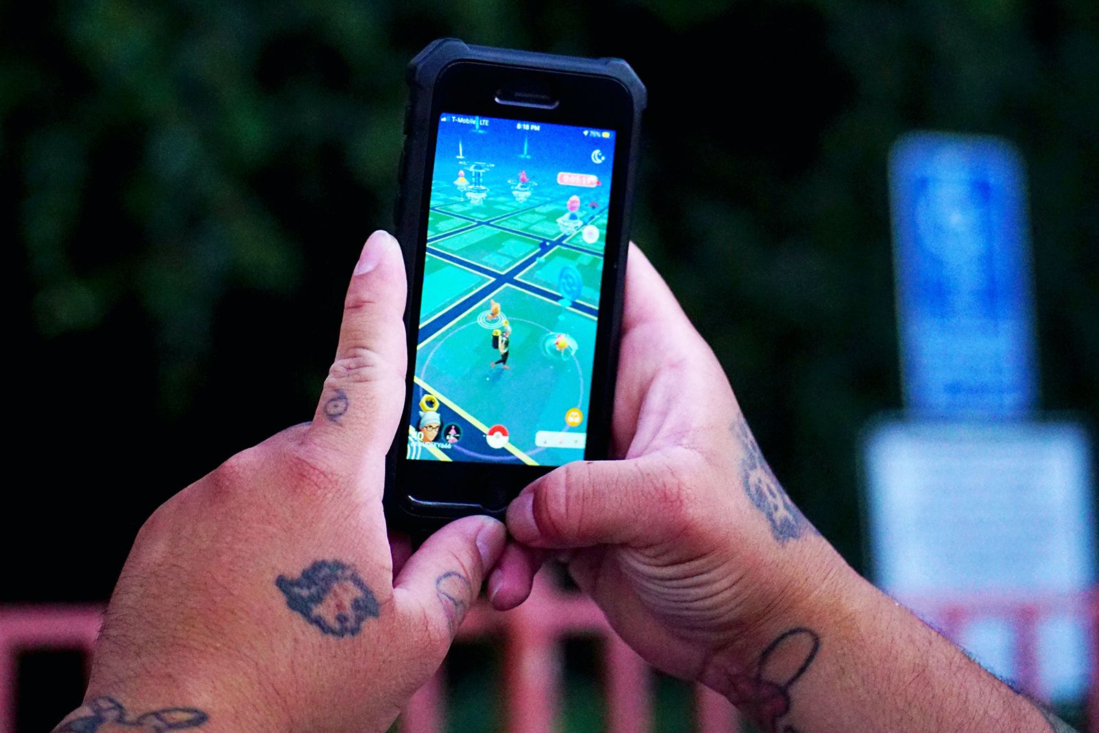 Tattooed hands hold a smartphone with Pokemon Go