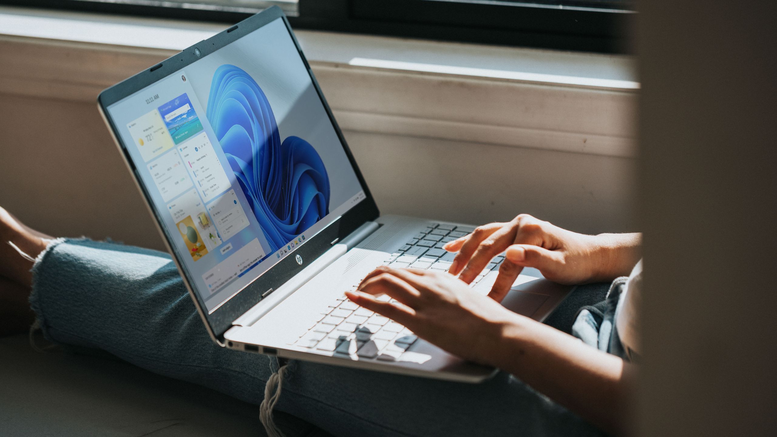 Close-up image of a person sitting in front of a window with legs stretched out and holding a laptop running Windows 11