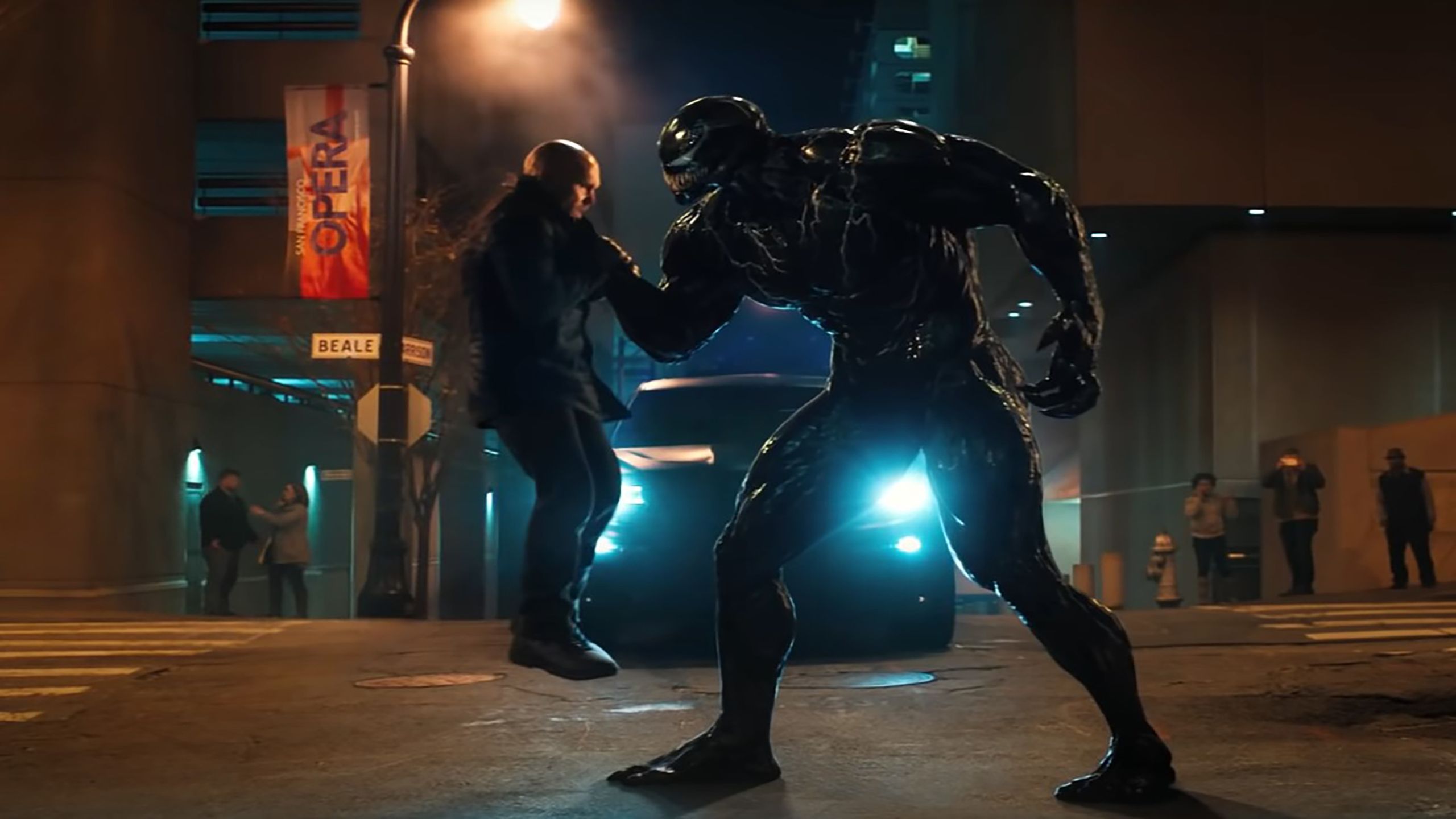 Venom holds a grown man by the neck in a city street. 