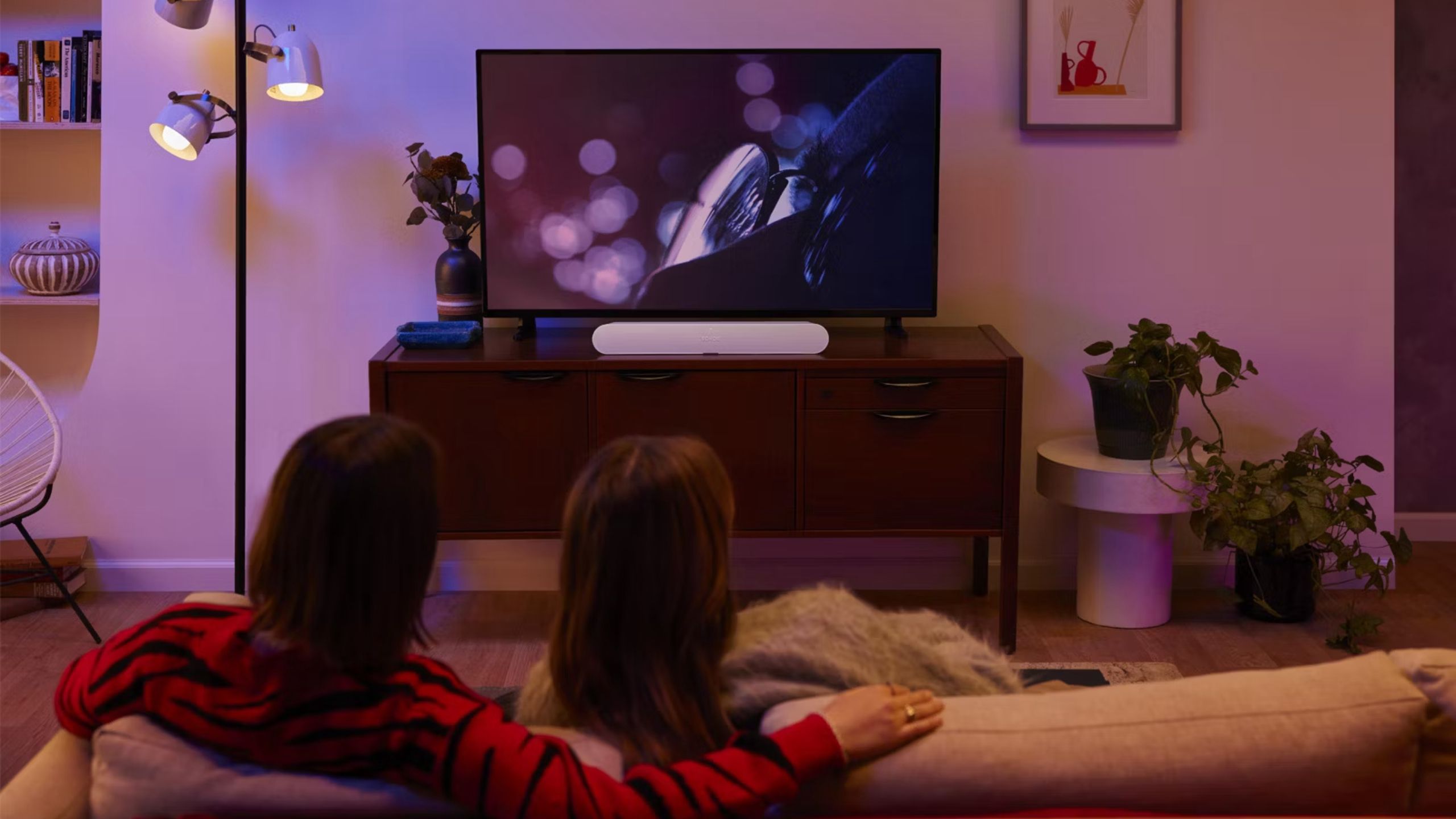 People sitting in a living room looking at a TV with a Sonos Ray.
