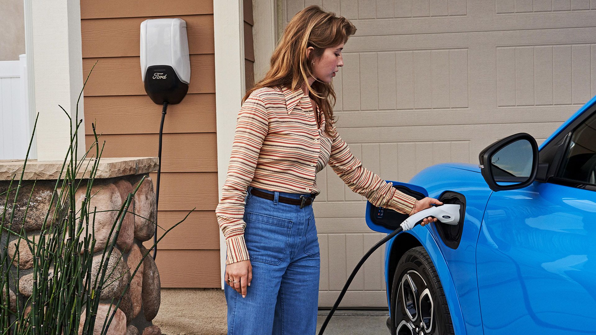 A woman charging a blue 2023 Mustang Mach-E GT from home.