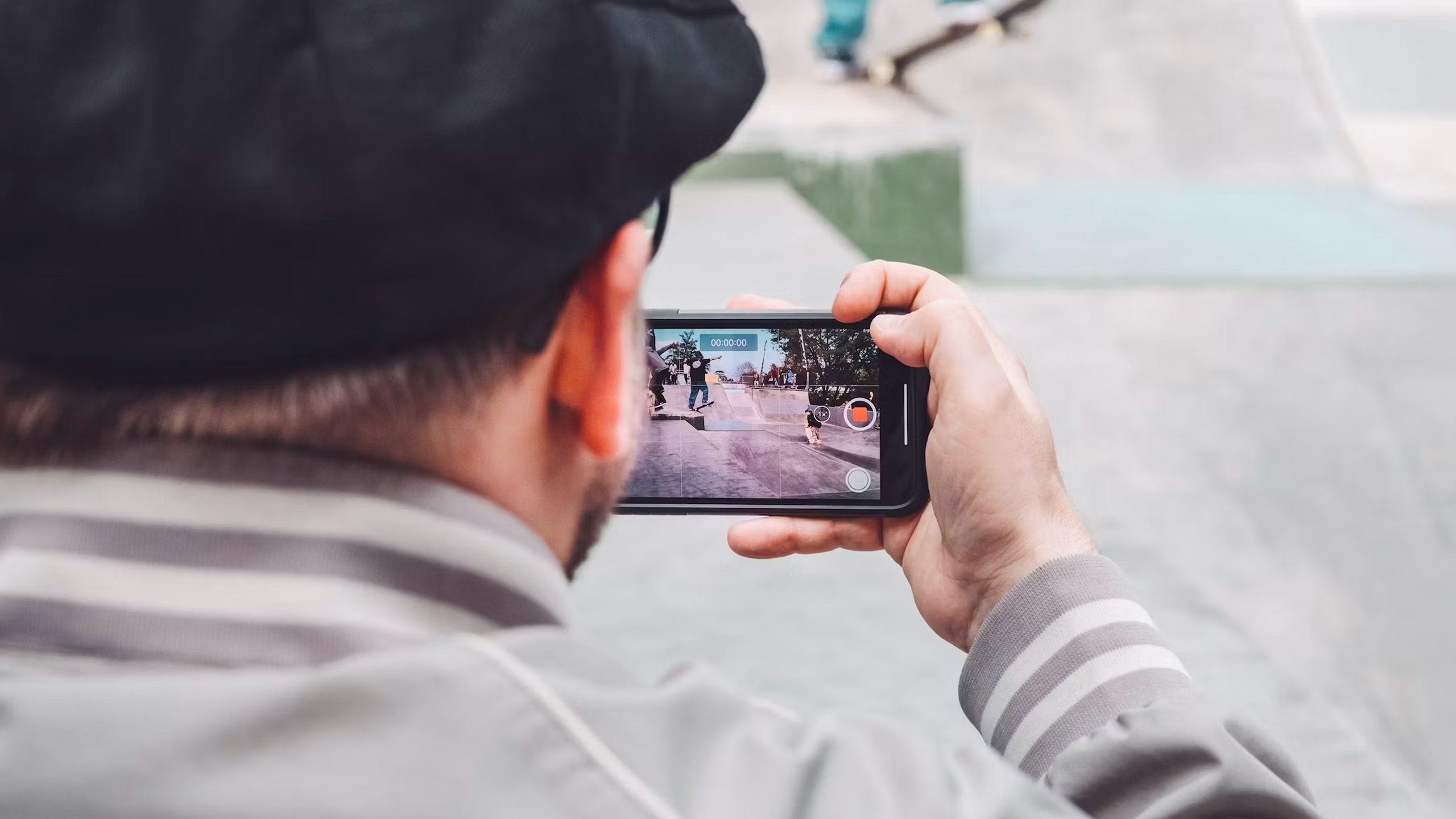 A man prepares to record a video with his phone of a skateboarder.