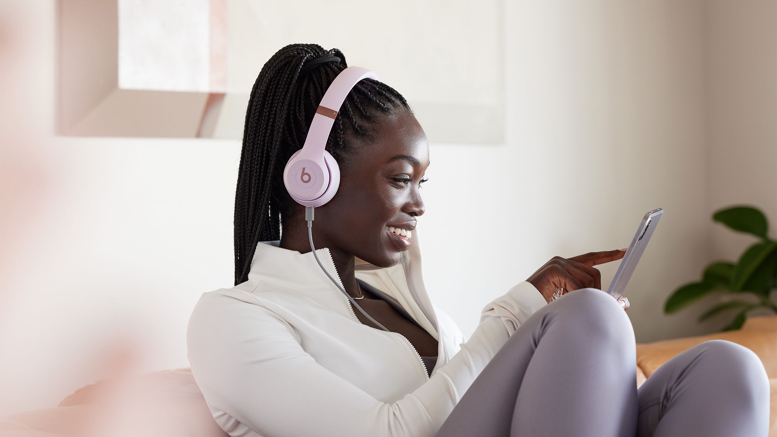 A woman sits on a couch with a pair of pink Beats Solo 4 headphones on. 