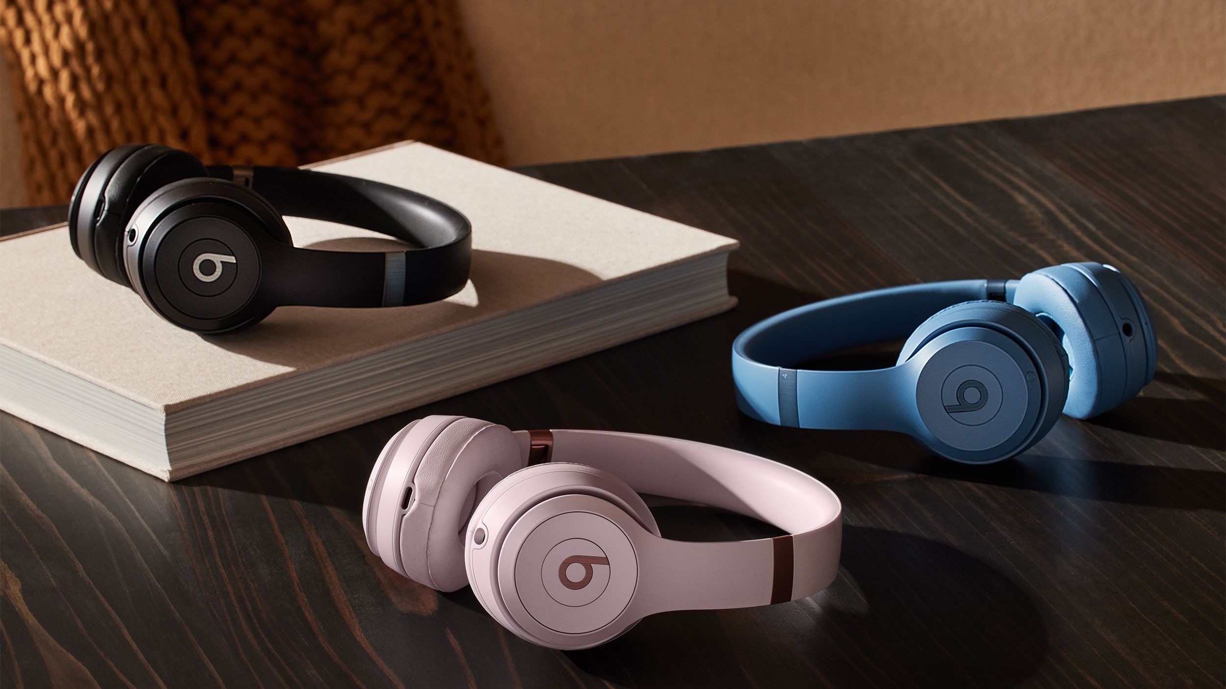 A pair of black, pink and blue Beats Solo 4 headphones sit on a table. 