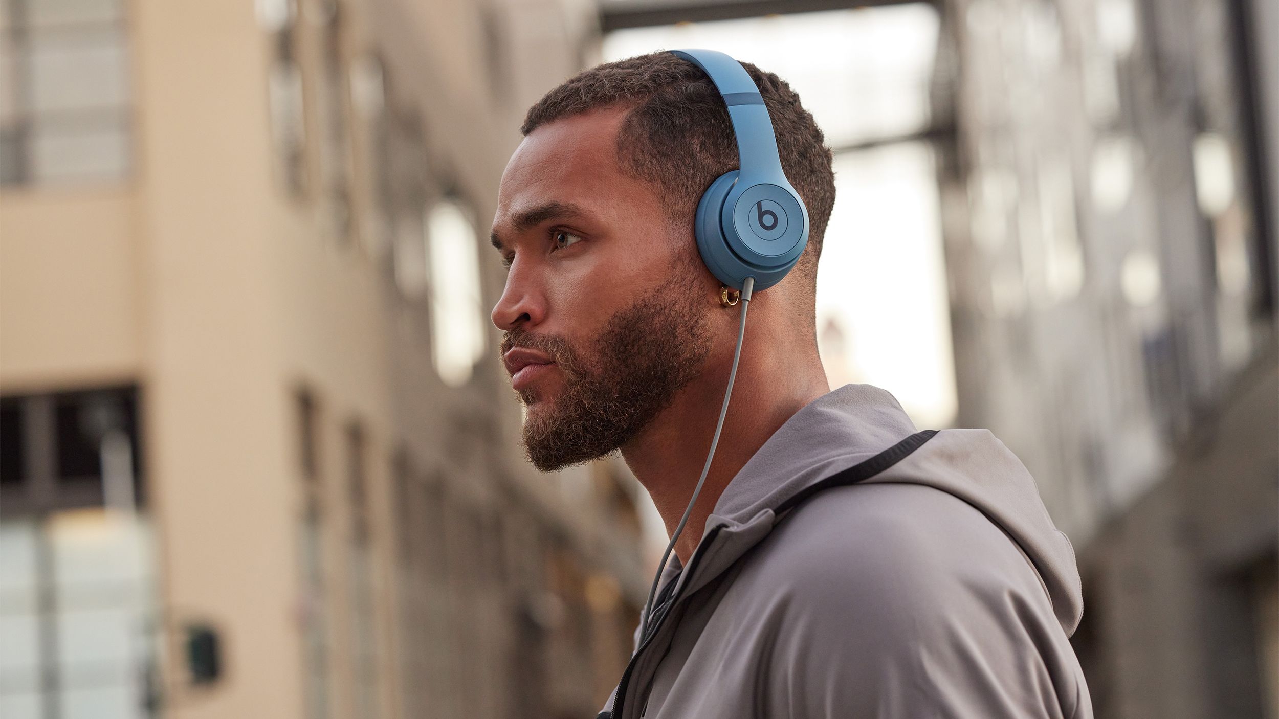 A man wears the Beats Solo 4 headphones in a city with the 3.5mm audio cable attached. 