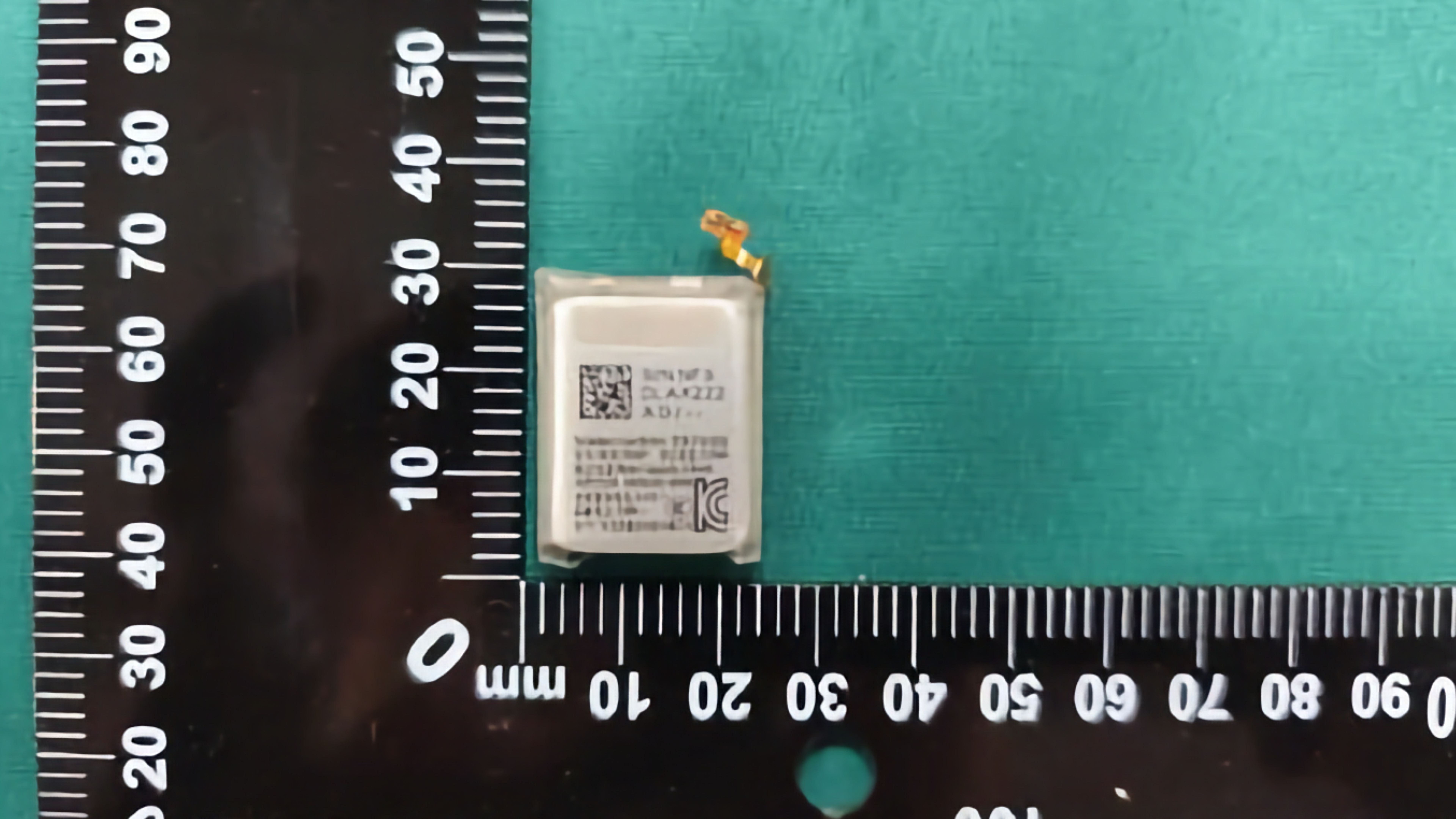 A small smartwatch battery next to some rulers