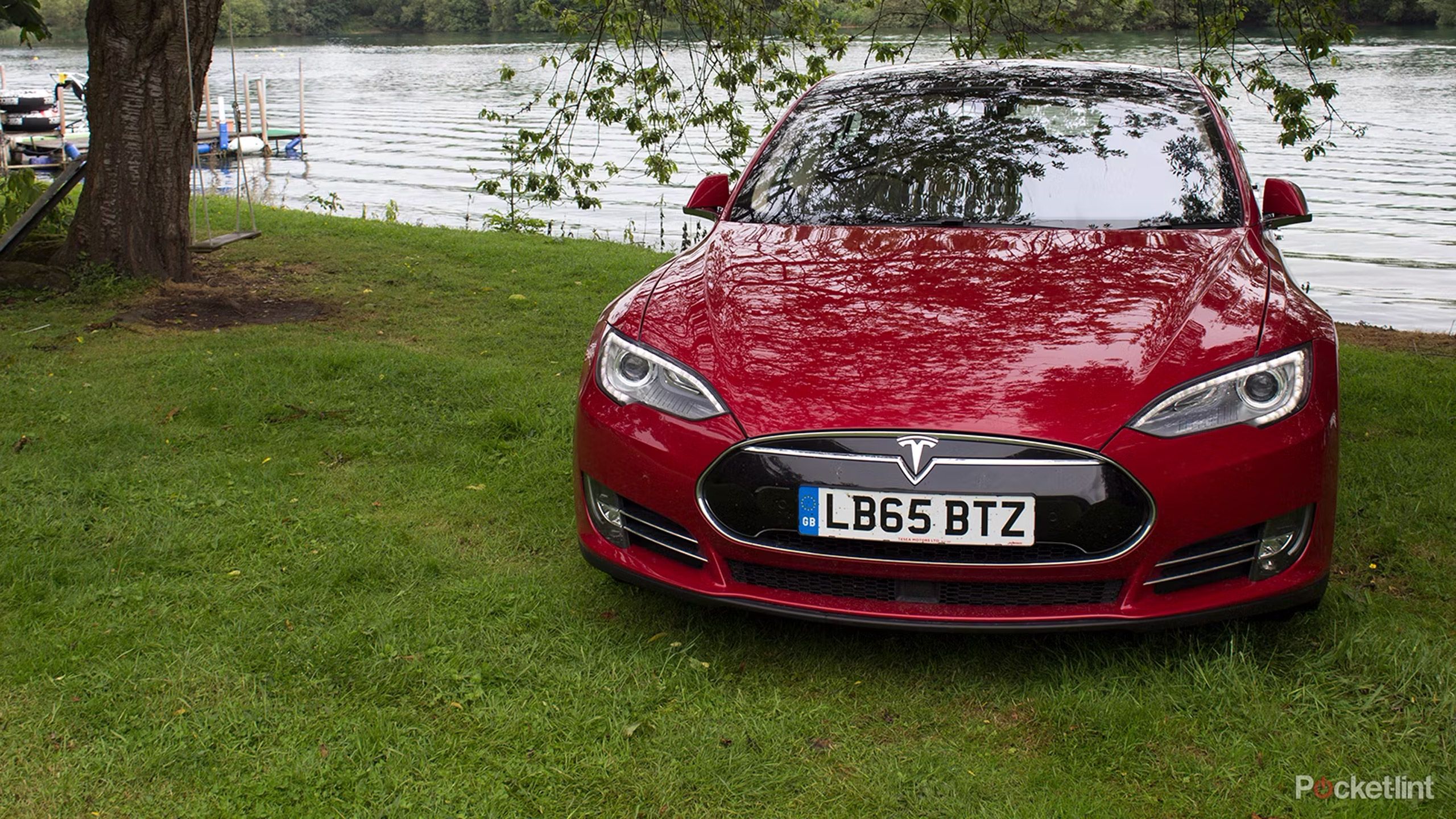 A red Tesla Model S sits by an English lakefront