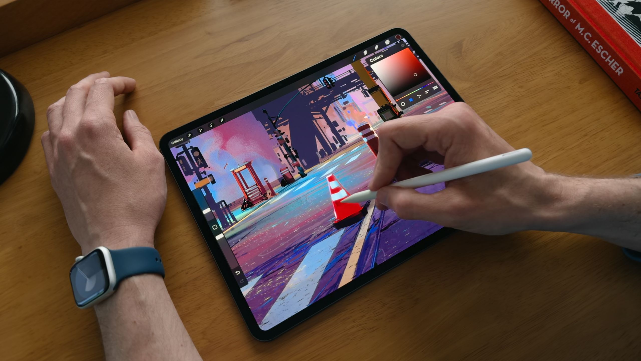 An Apple iPad Pro sits on a desk with a hand holding the Apple Pencil Pro. 