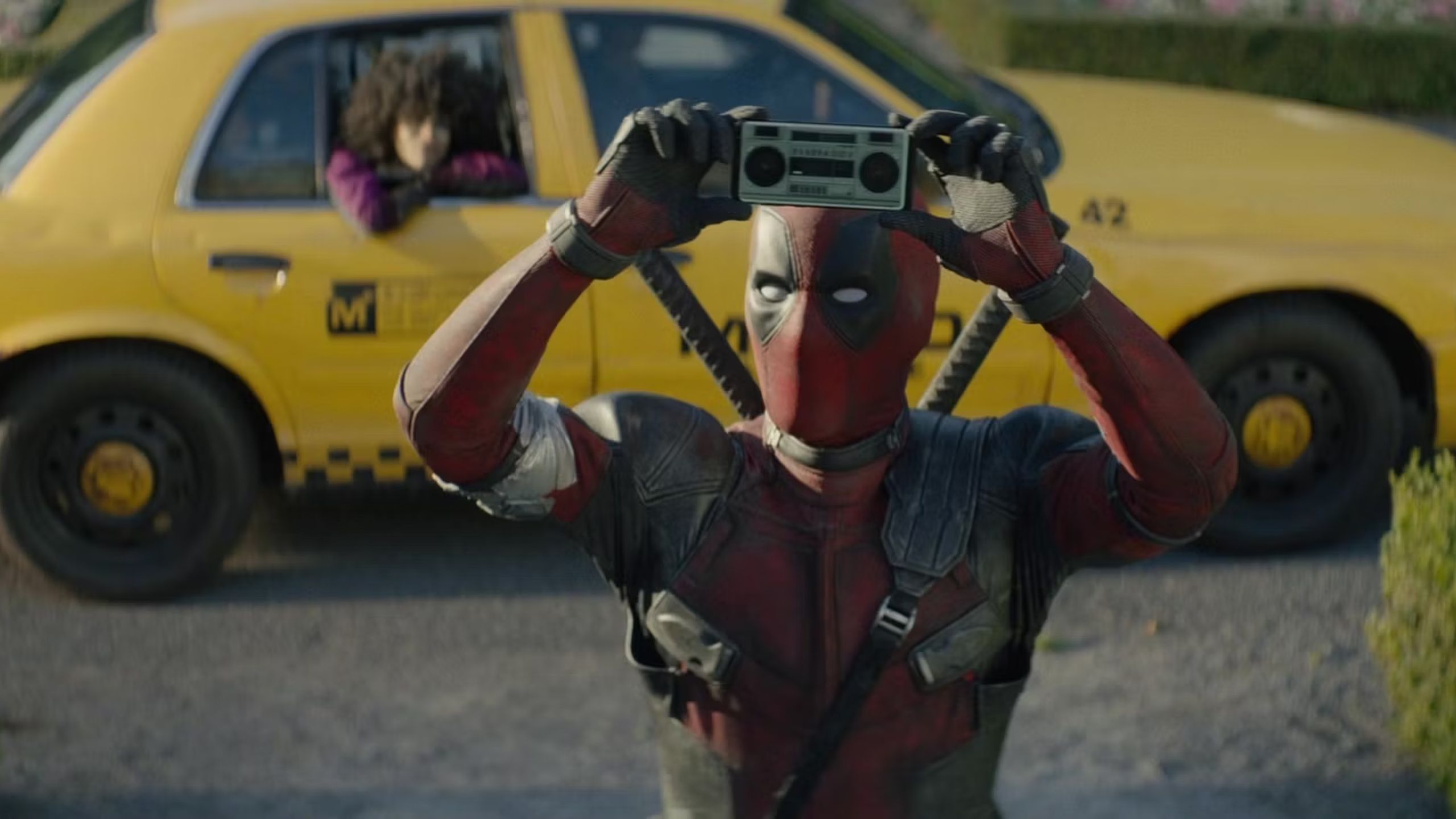 Deadpool holding a cassette tape in front of a taxi