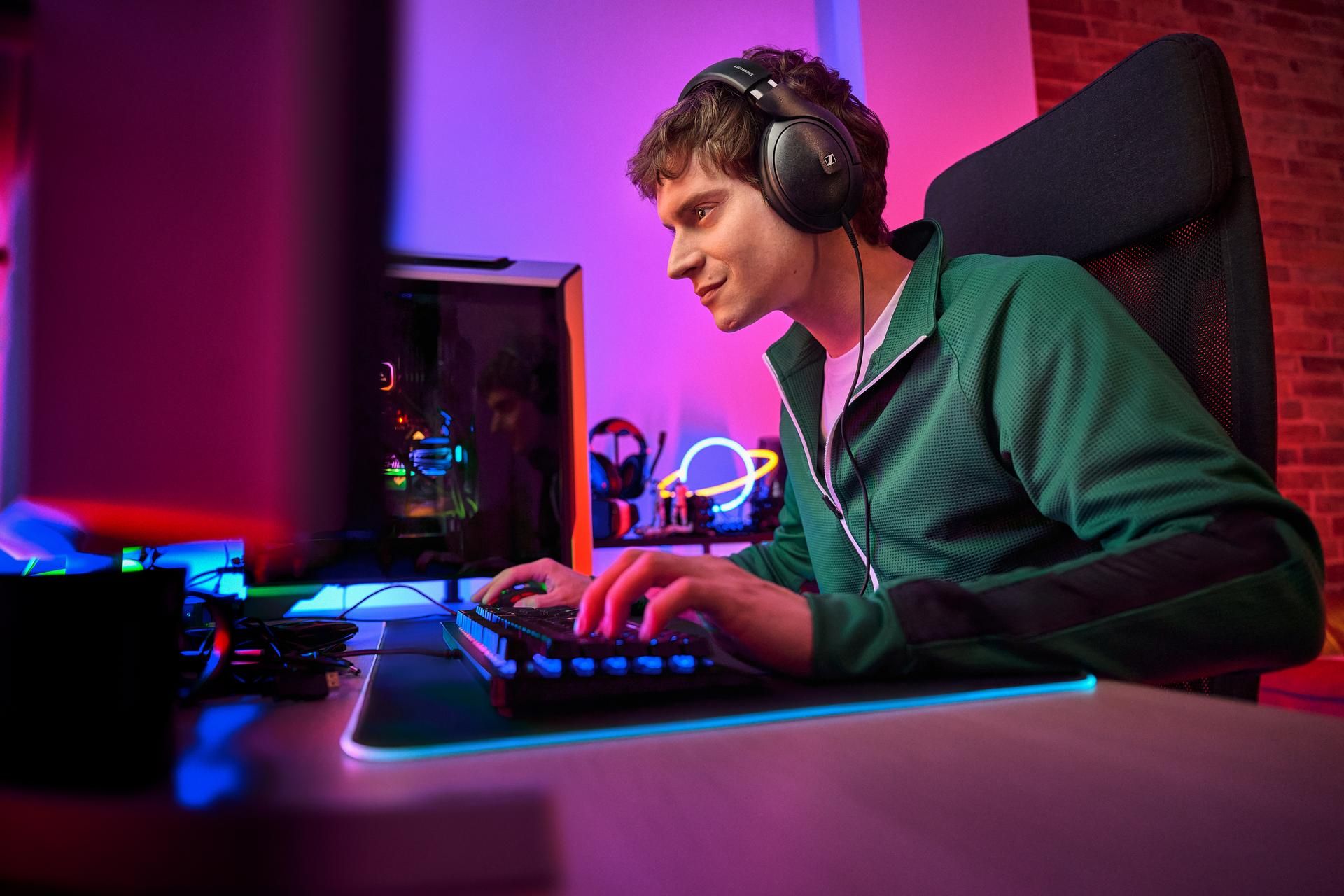 A person sitting at a desk gaming on a PC while wearing the Sennheiser HD 620S headphones.