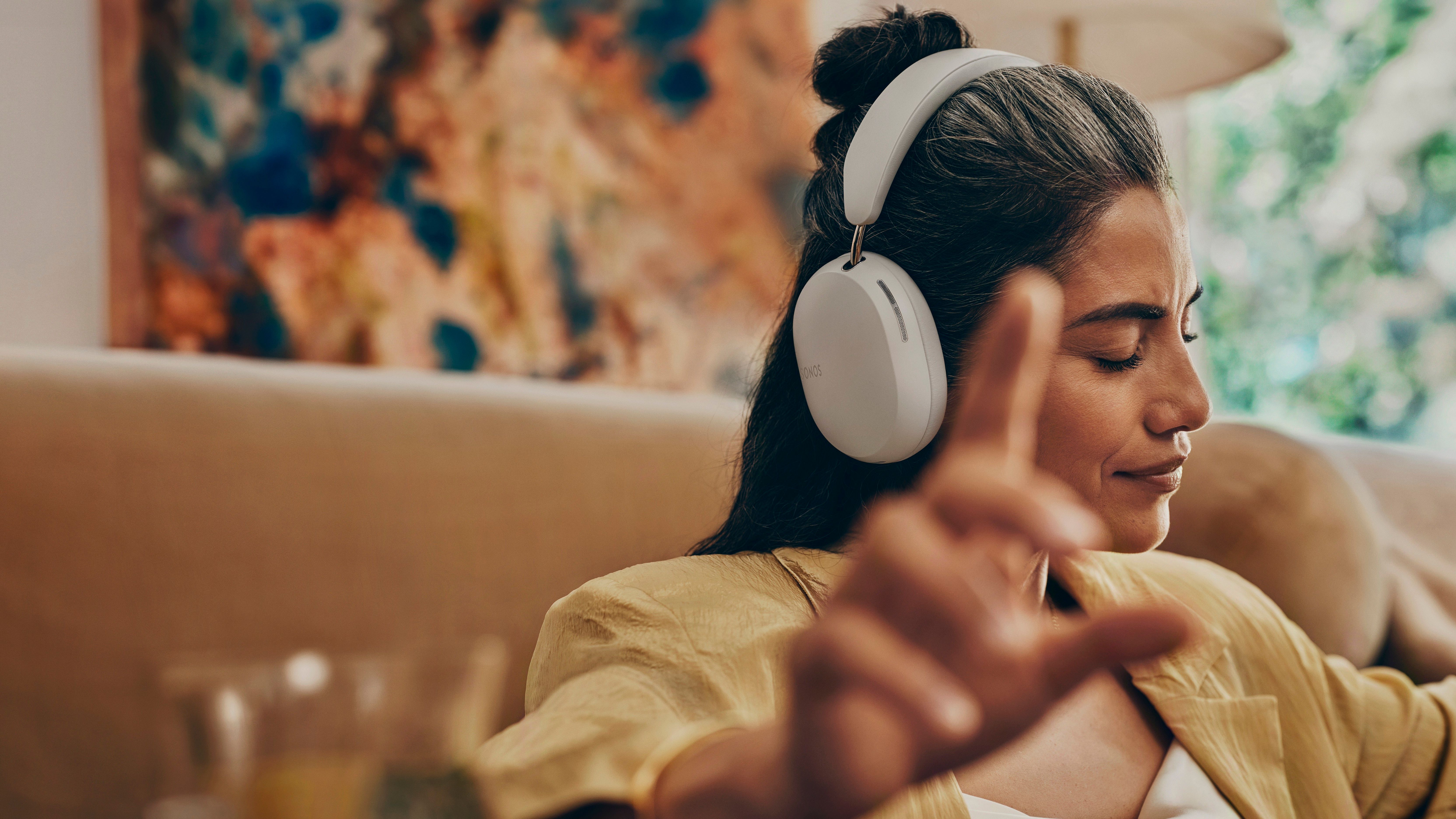 A woman wearing a white pair of Sonos Ace while holding her hand up toward the camera