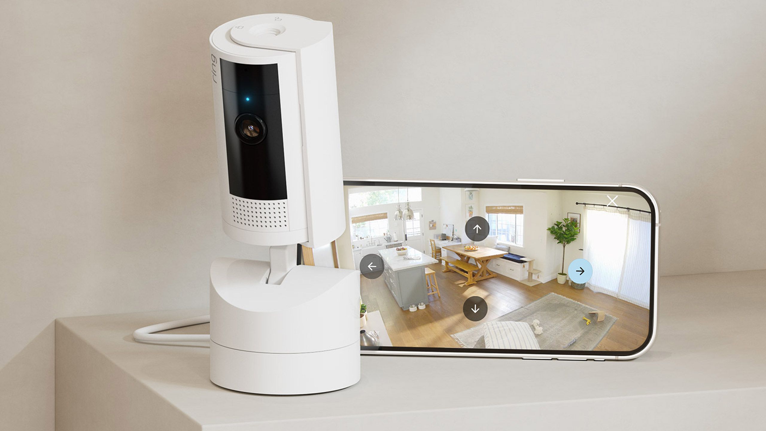 A white Ring Pan Tilt Indoor Cam sits next to the Ring app