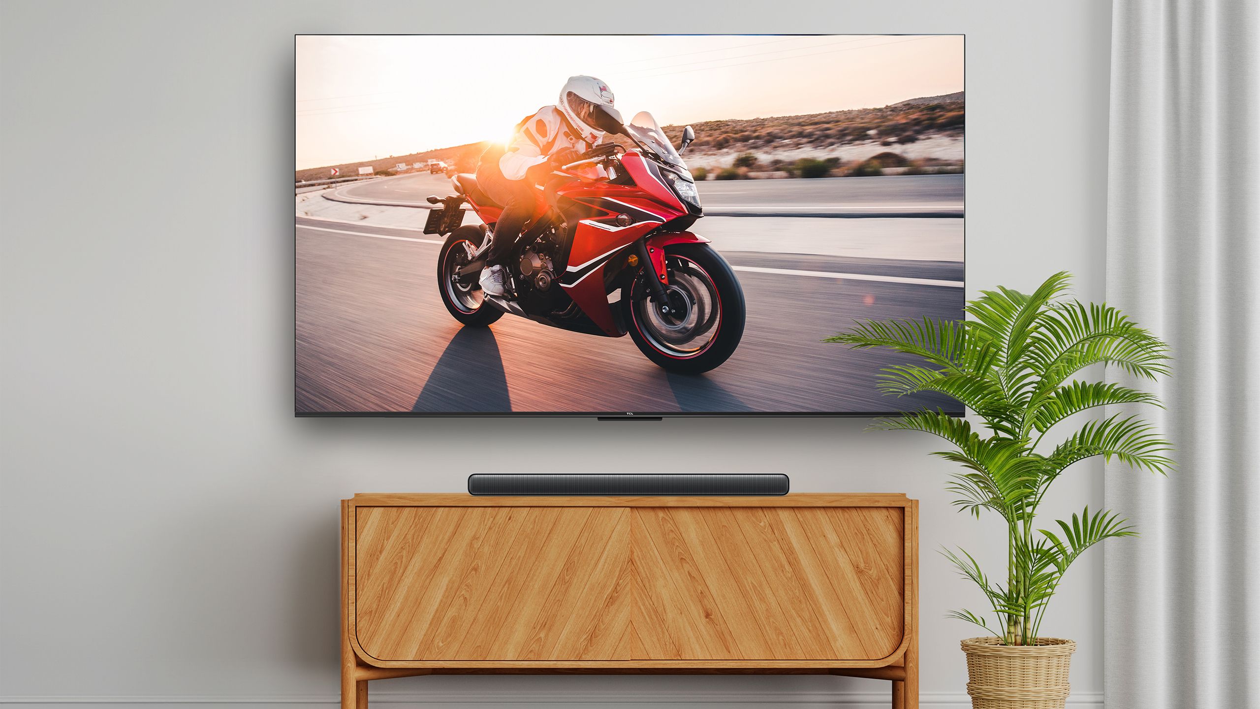 The TCL S45H soundbar on a table below a TV with a motorcycle video on the screen. 