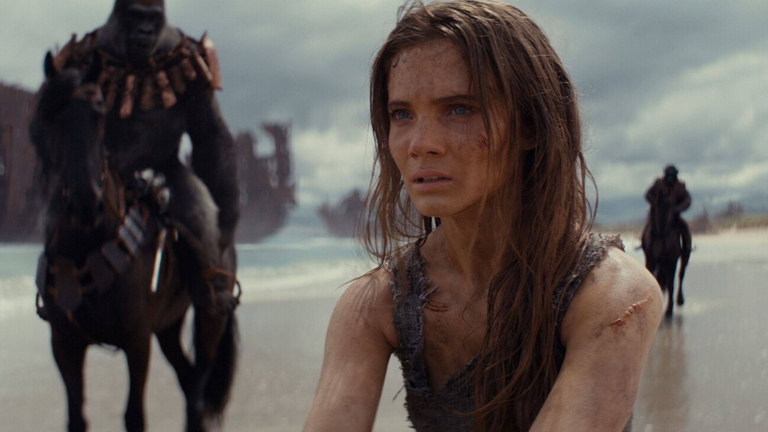 A woman on a beach surrounded by apes on horseback. 