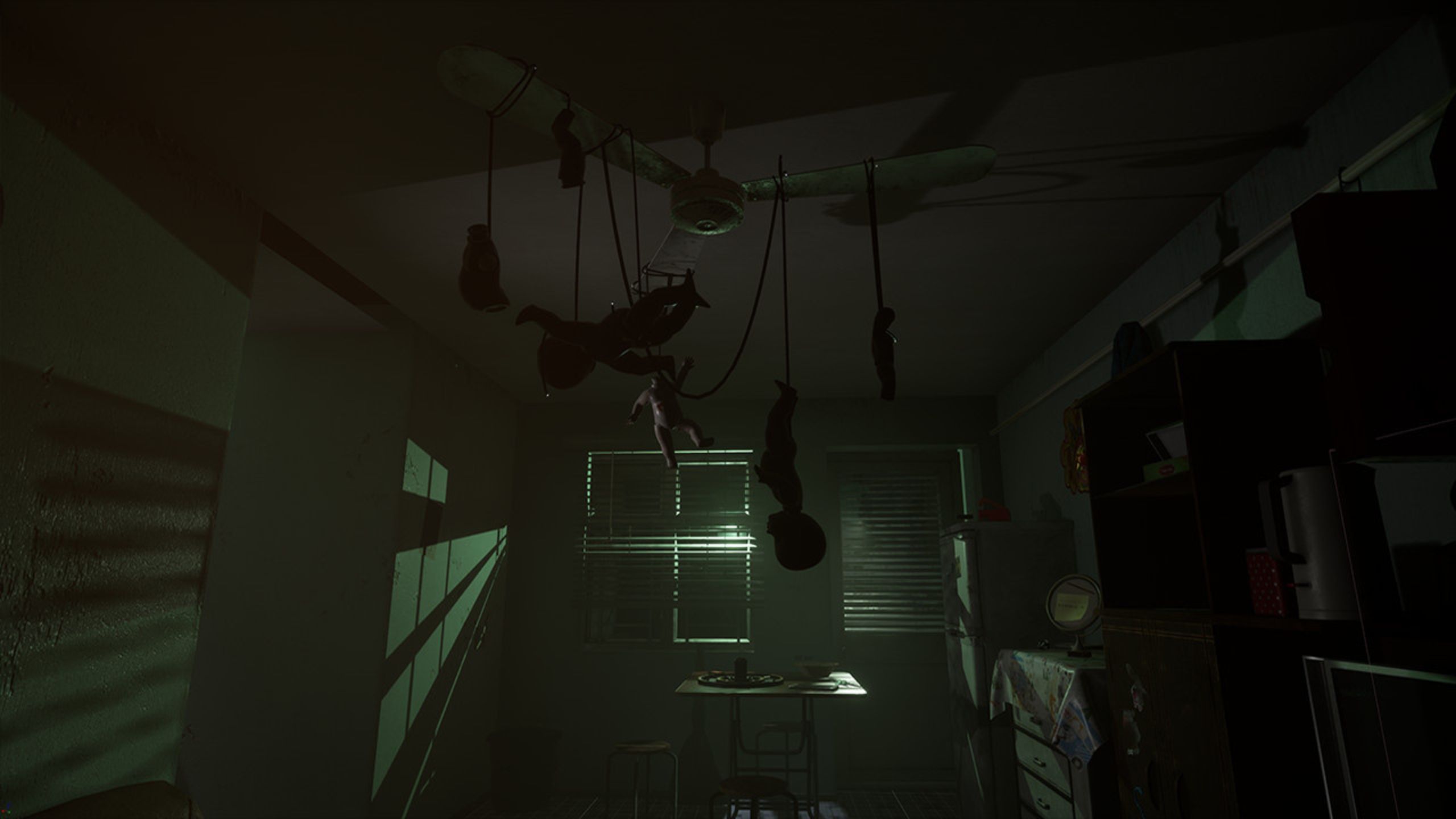 A shadowy room with dolls hanging from a fan.