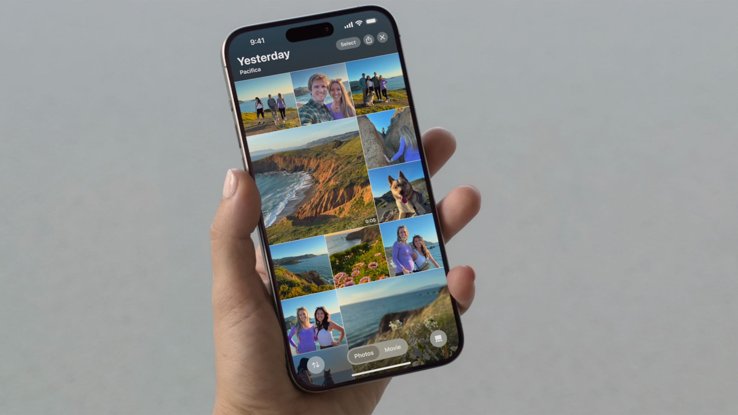 A hand holds an iPhone with the new Photos app above a gray background. 