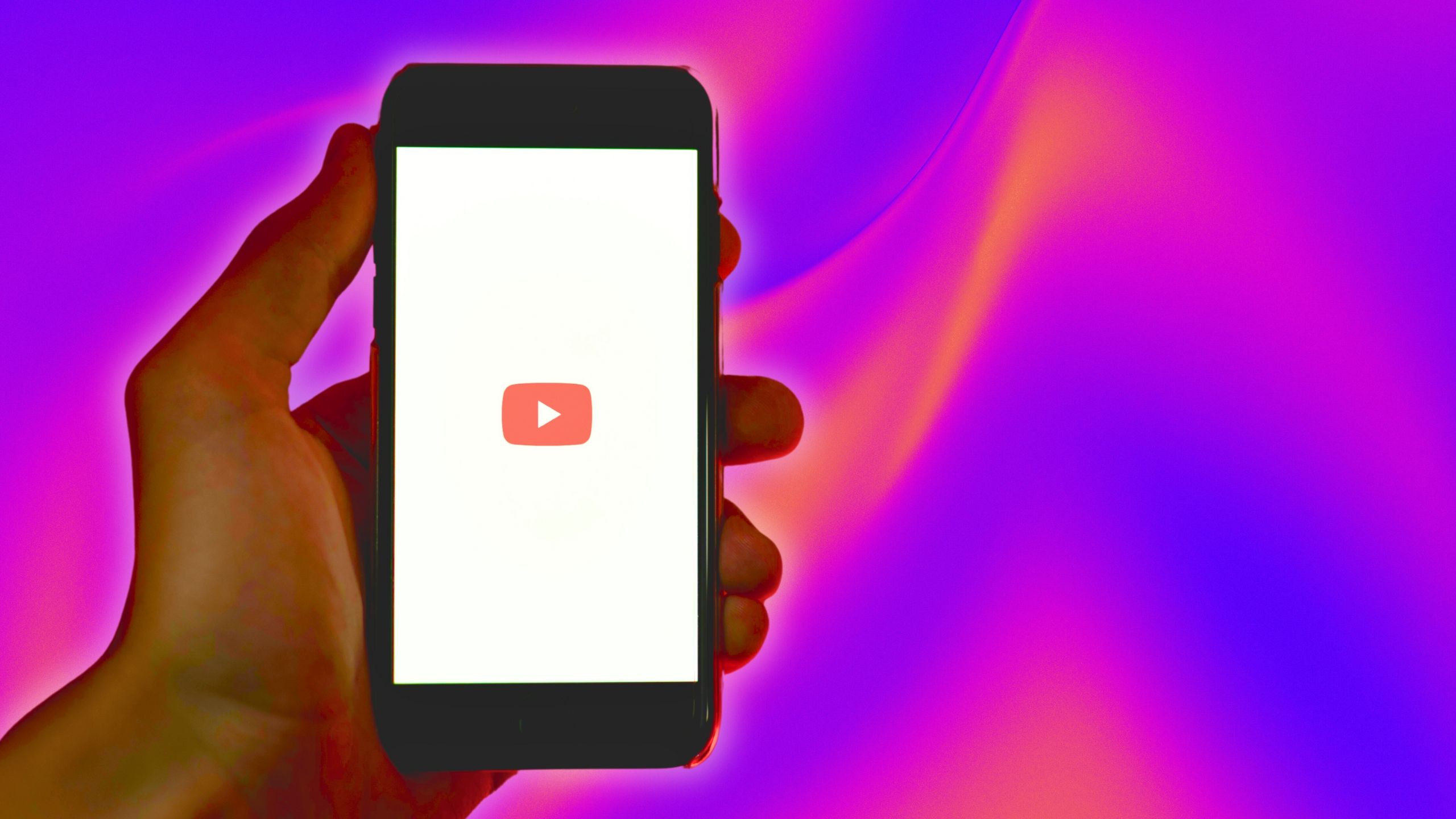 YouTube on a hand-held iPhone against a pink and purple background. 