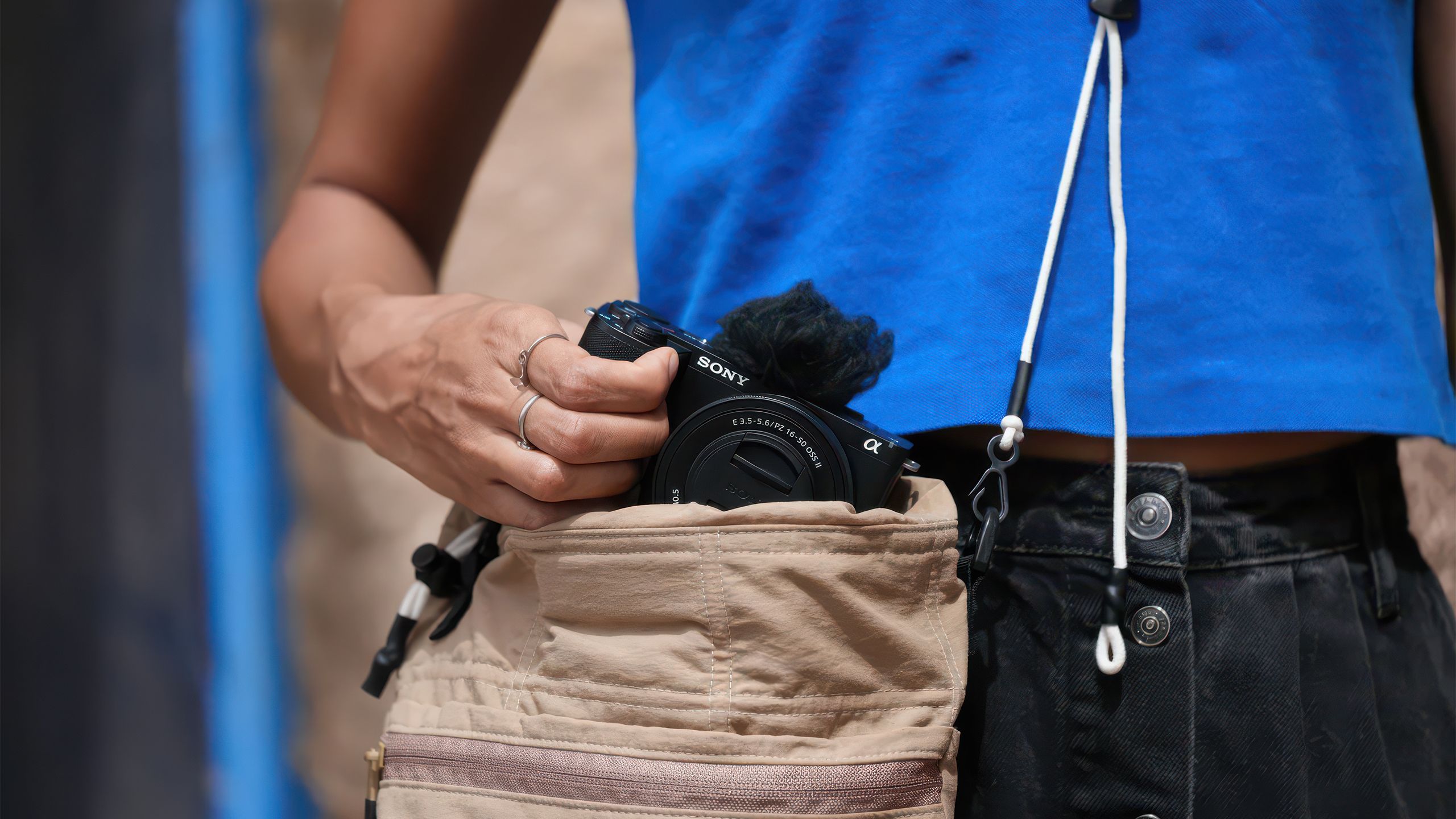 A hand pulls the Sony ZV-E10 II camera out of a bag hanging at their hip. 