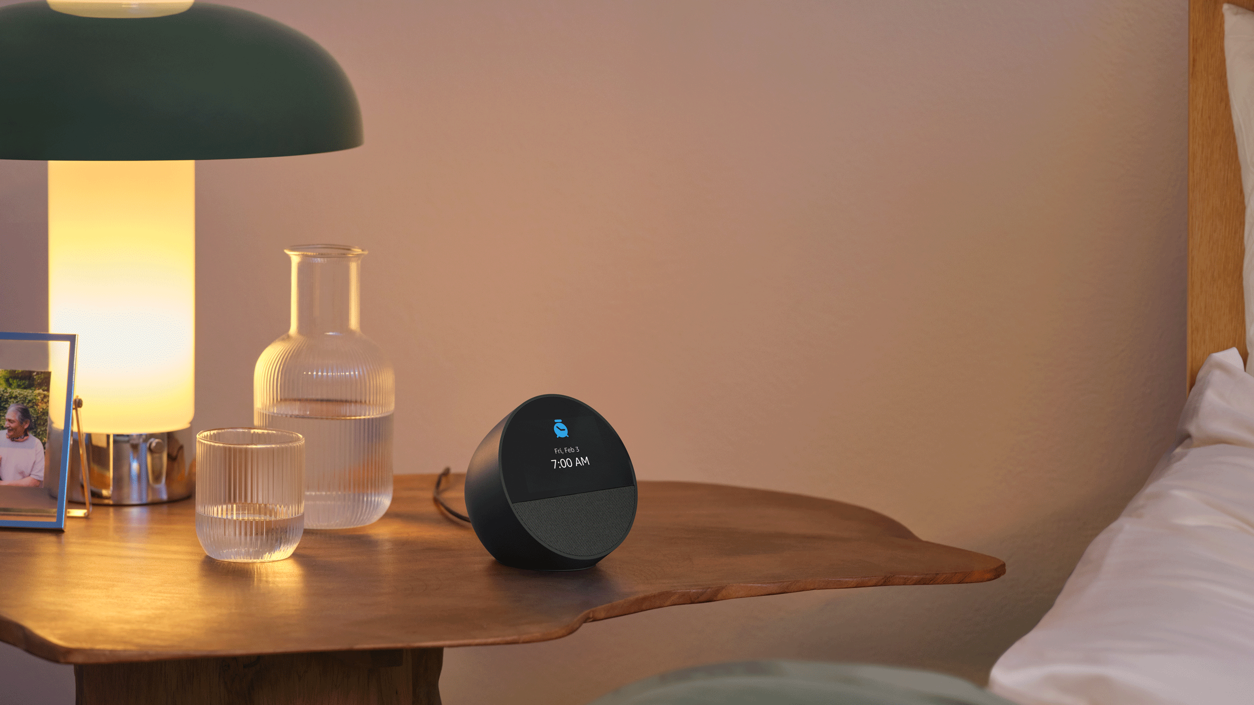 A black Echo Spot sits on a wooden bedside table