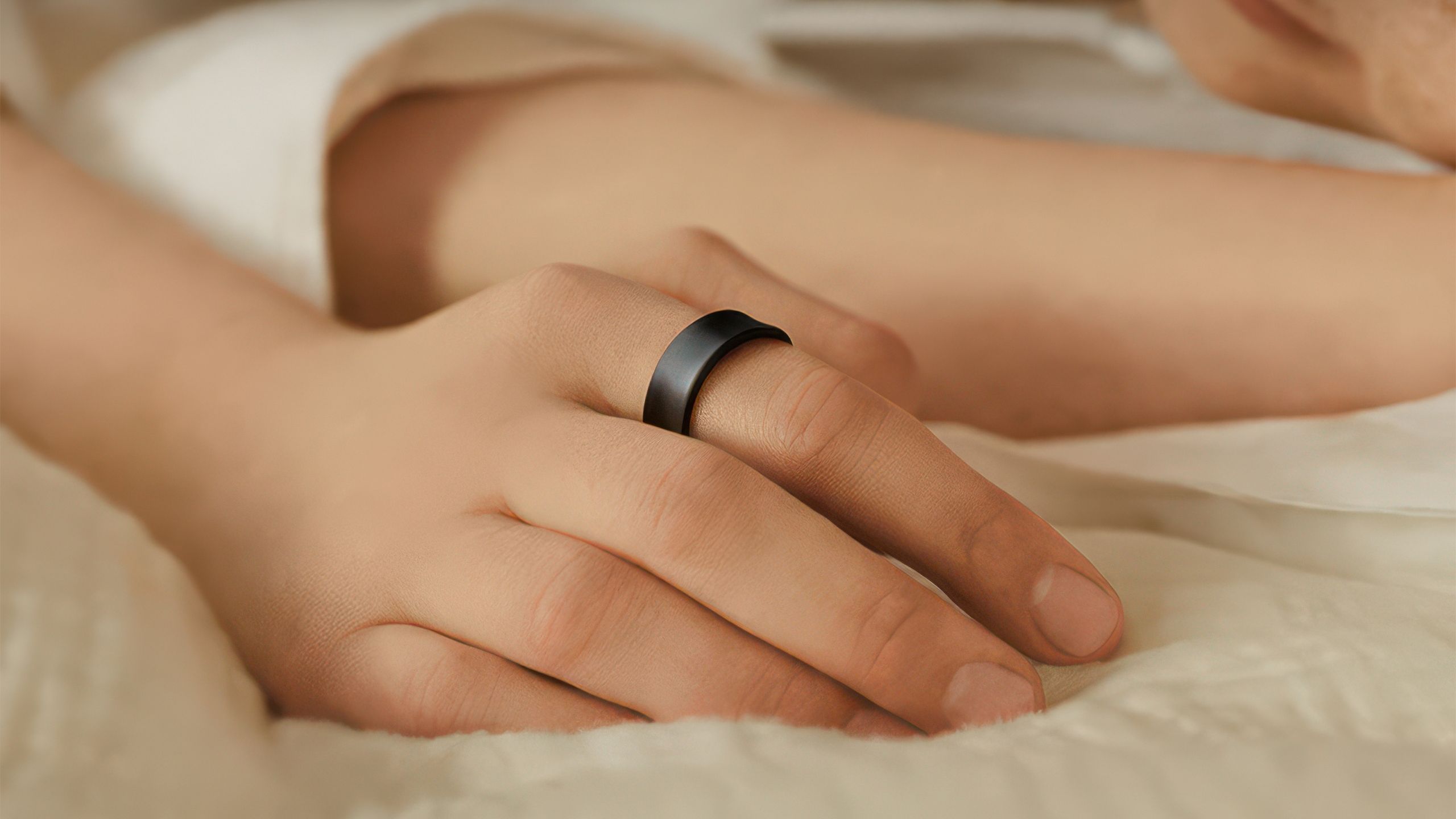 A hand with the Samsung Galaxy Ring rests on a bed. 