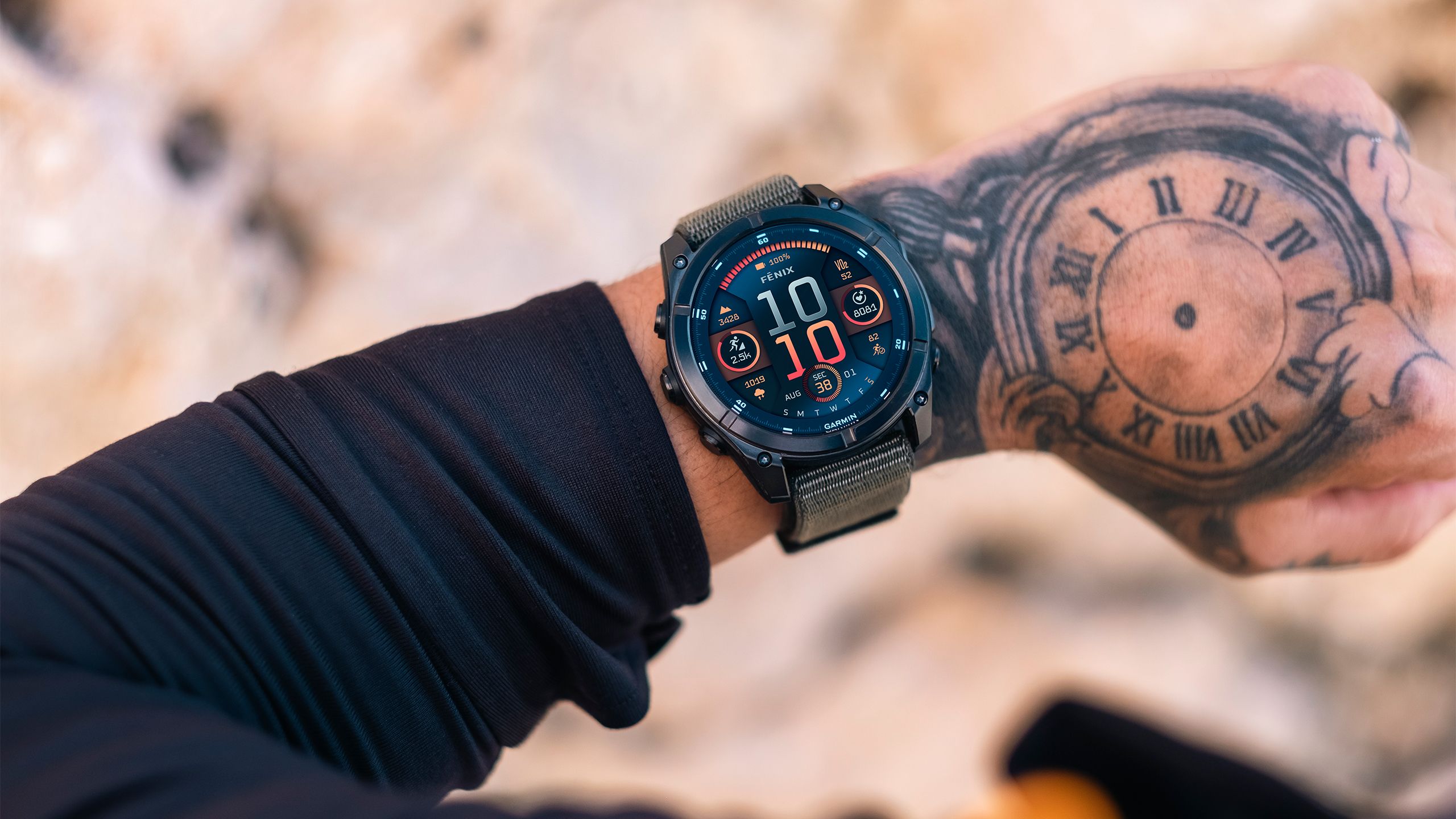 A wrist is held out over blurred rocks with the Garmin fenix 8 watch on it. 