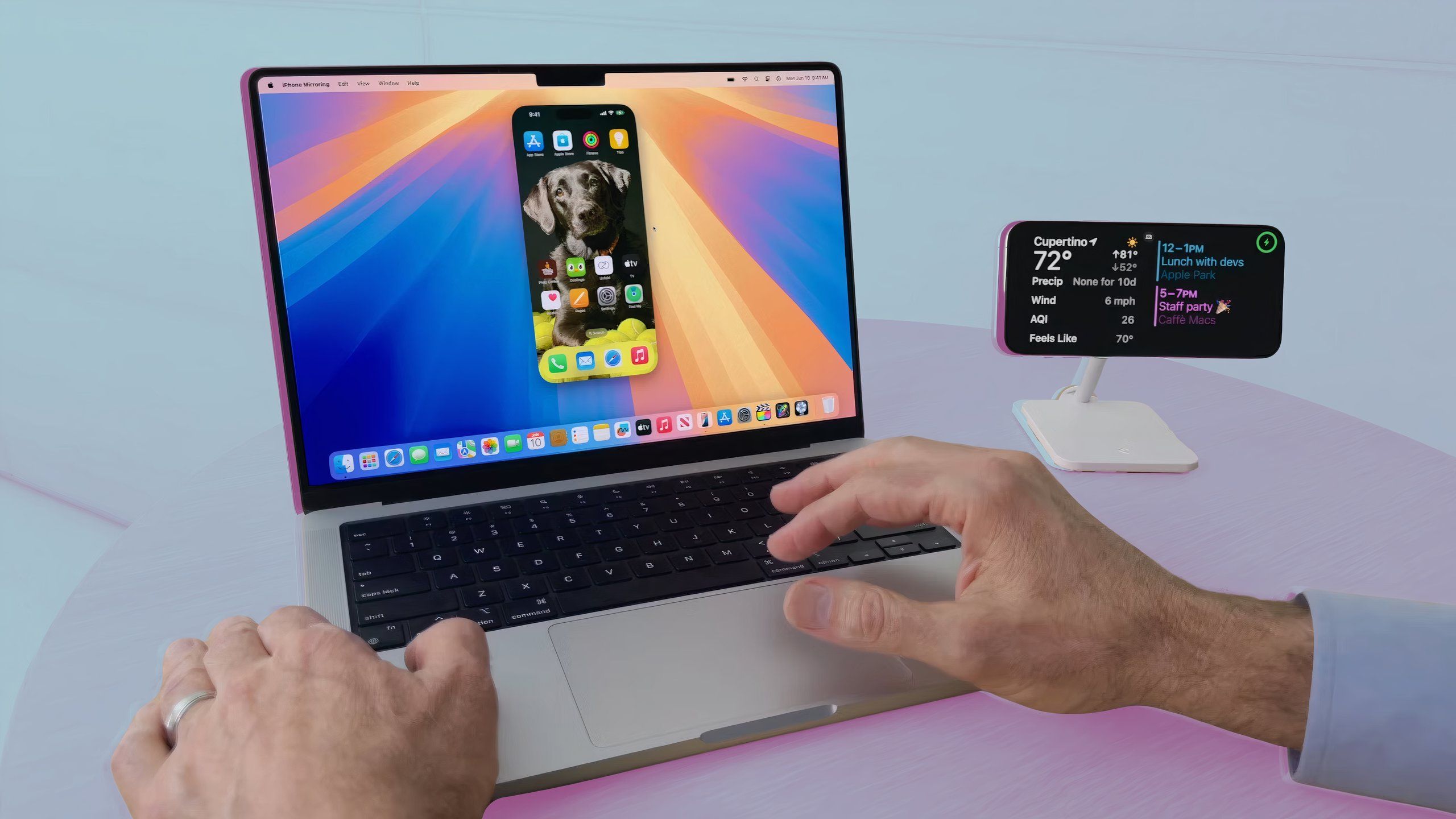 Craig Federighi's hands navigating iPhone Mirroring on a MacBook Pro, next to a docked iPhone.