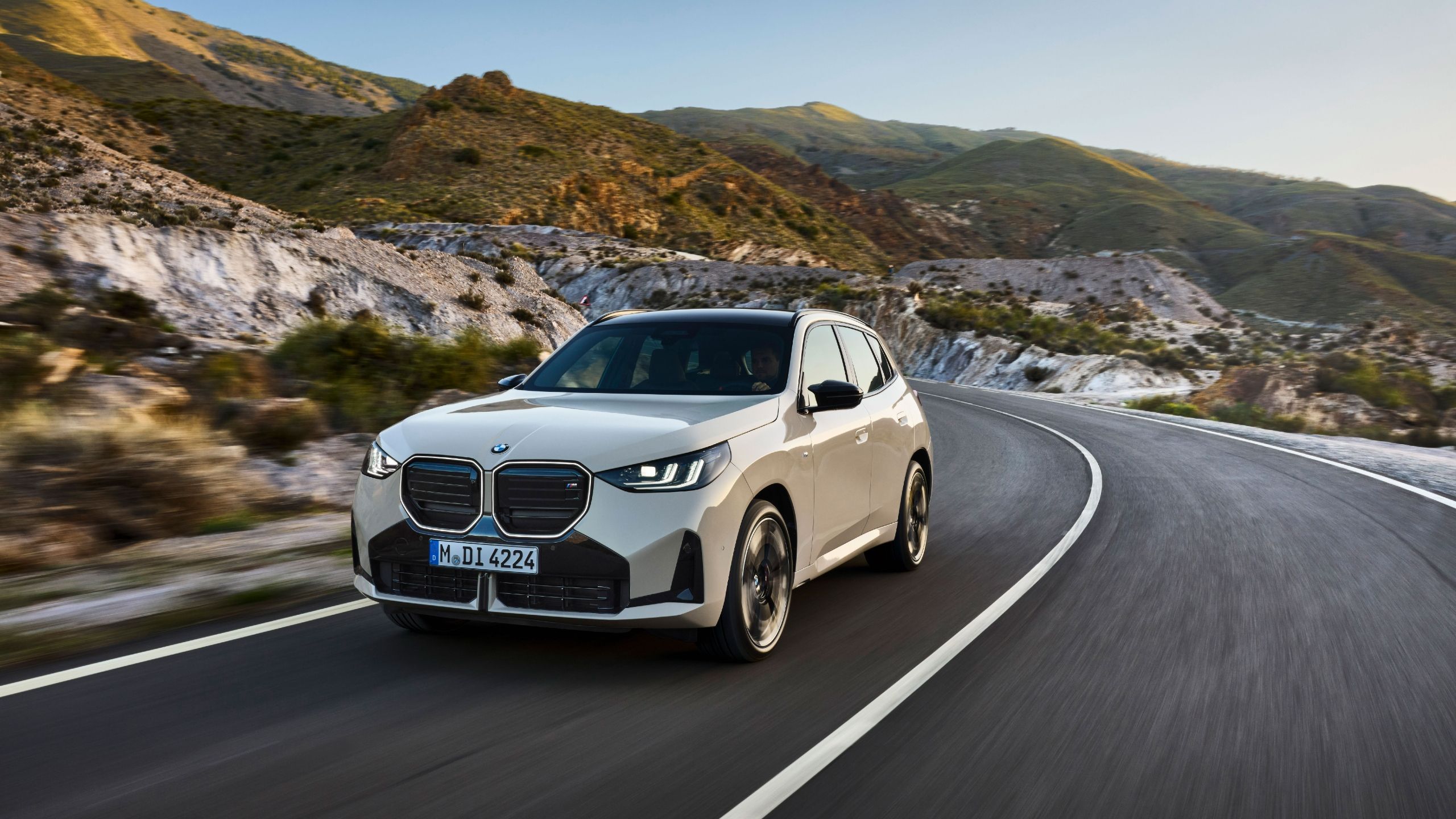Front quarter view of the 2025 BMW X3 M50 hybrid driving on road.
