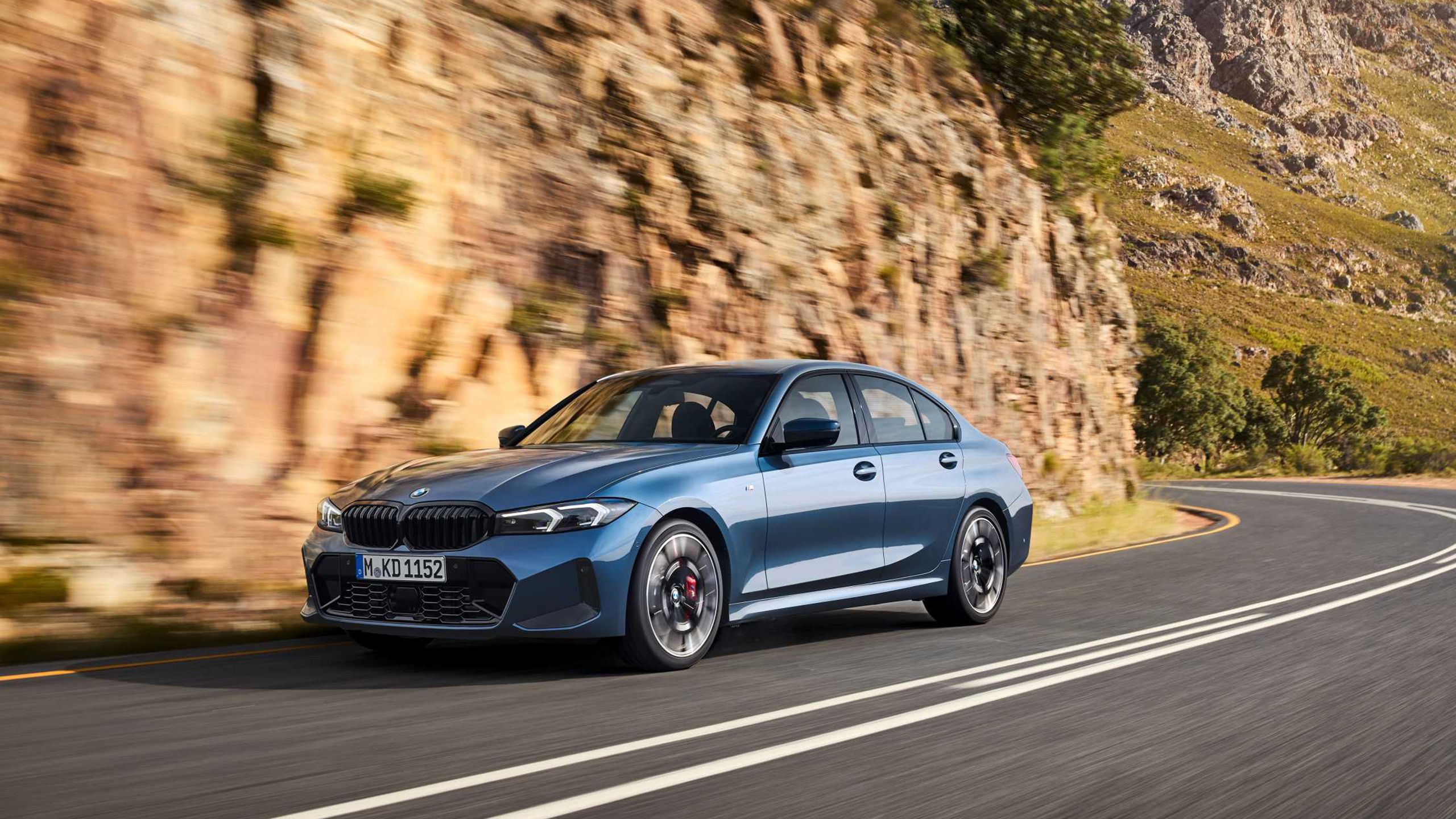 A 2025 BMW 3-series driving on a scenic road. 