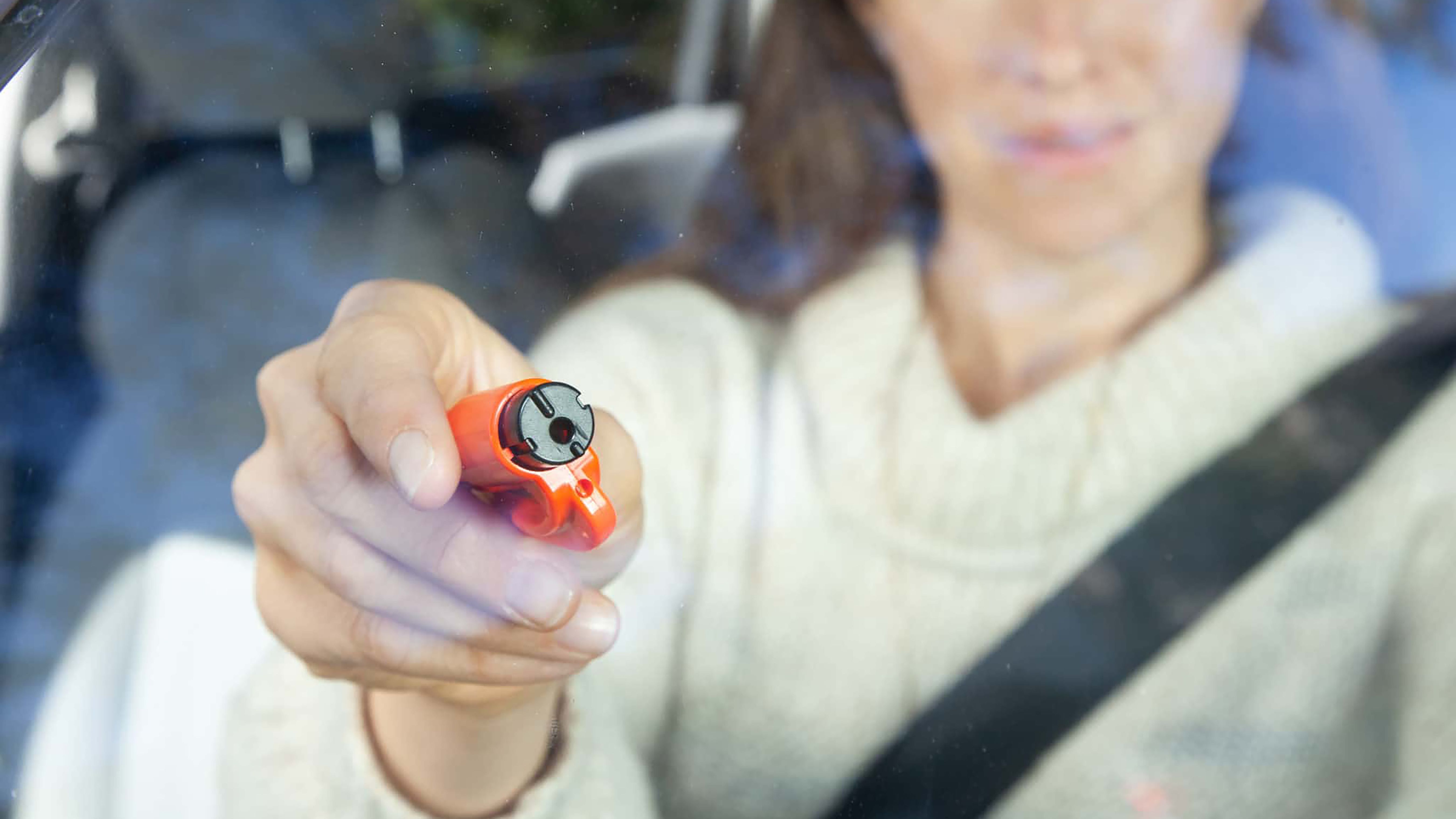 A woman holding a Resqme glass breaker tool to a window. 