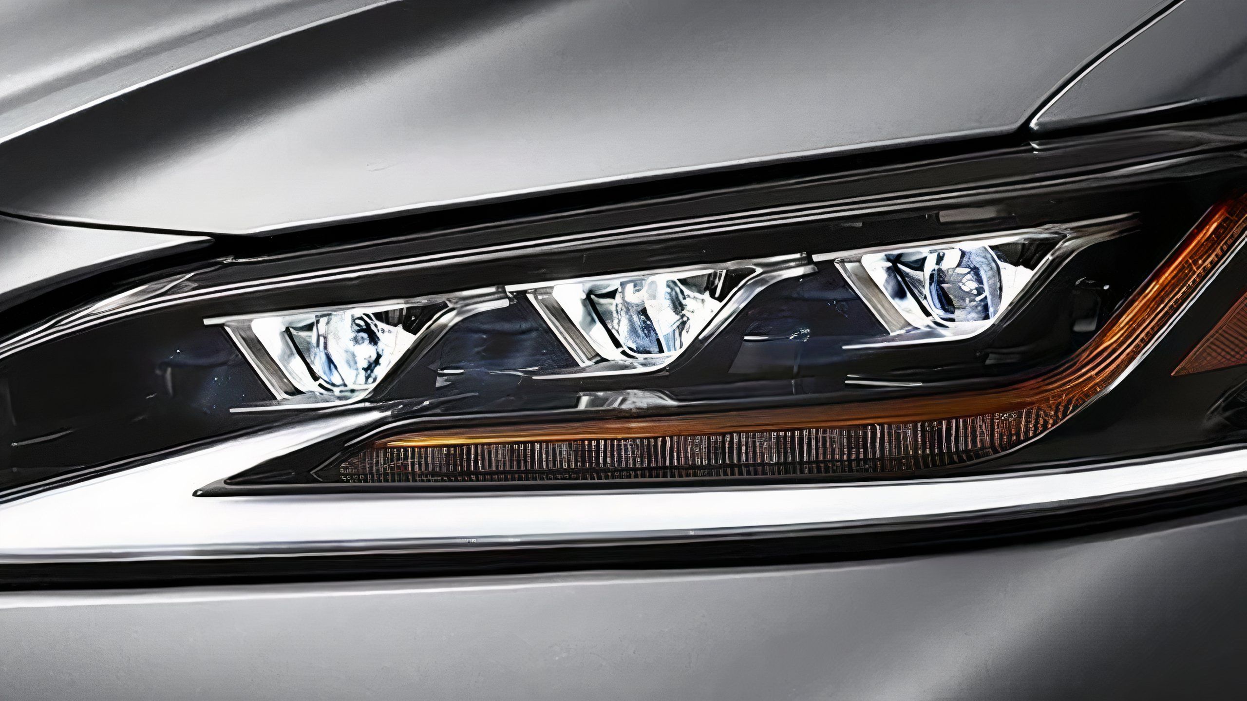 A still photo of Lexus triple beam headlights on a silver car. 