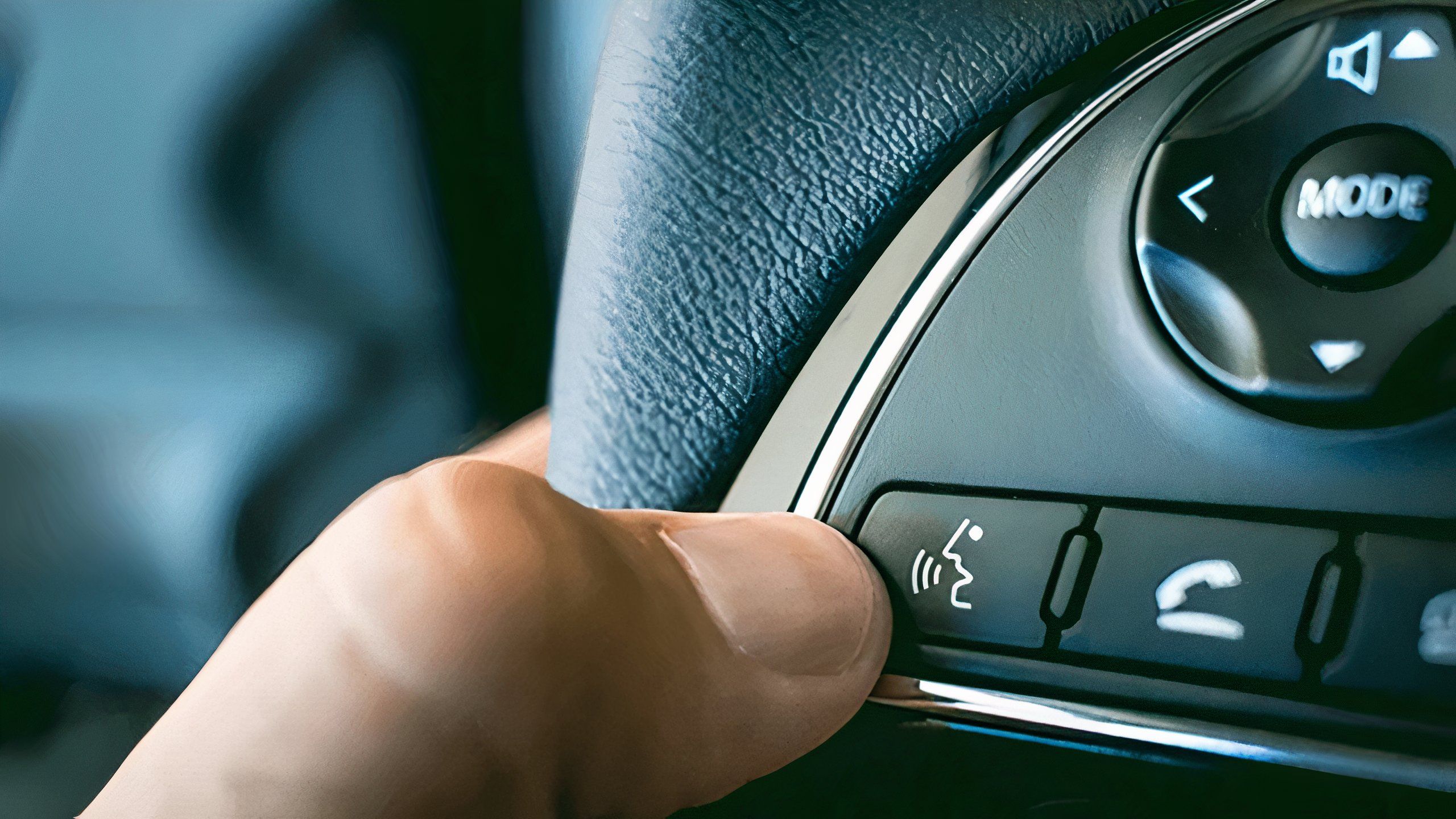 A still photo of a hand activating voice assistant button in a car. 