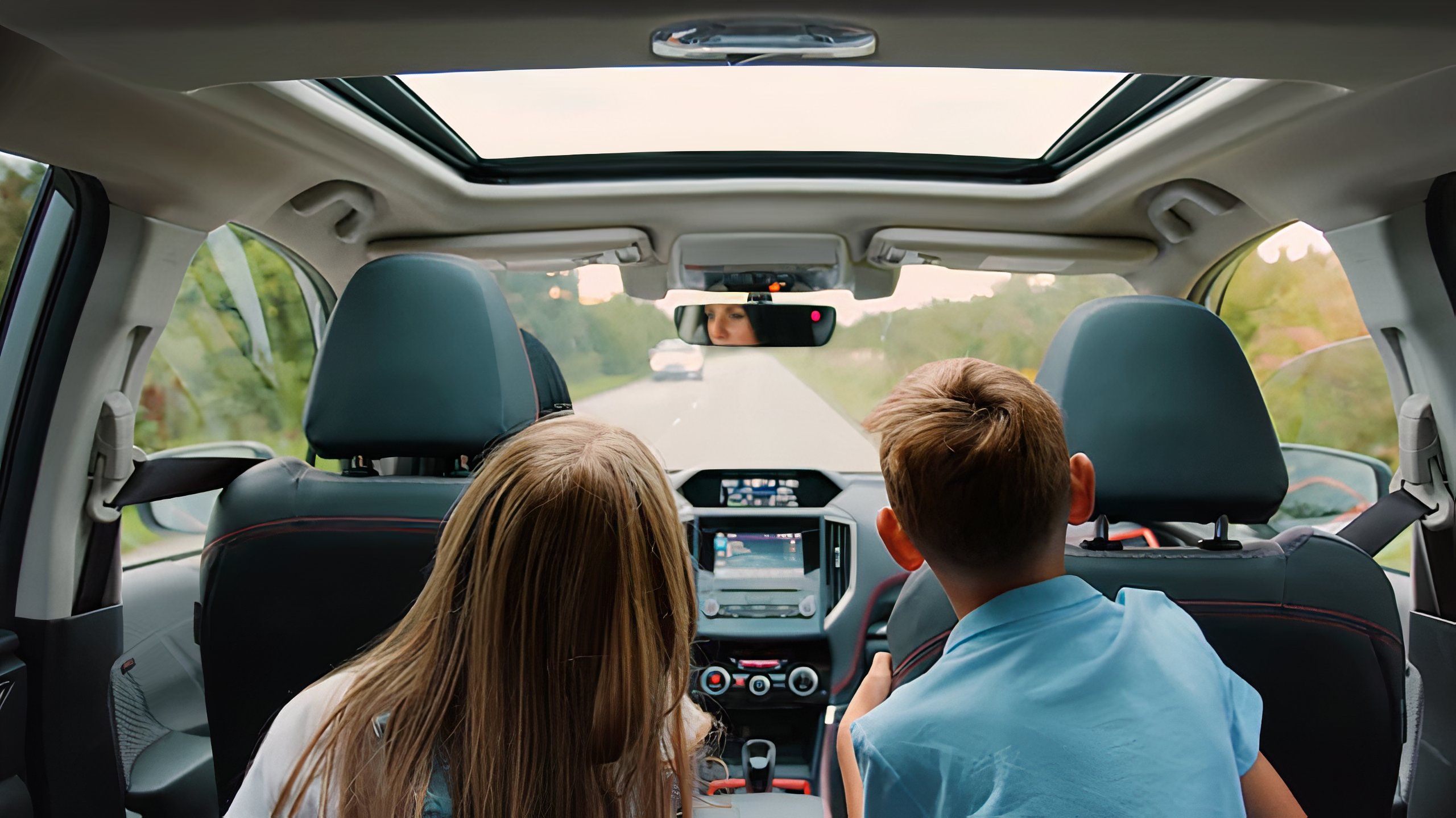 Two children lean forward from the pack seat to ask the driver of a car a question.