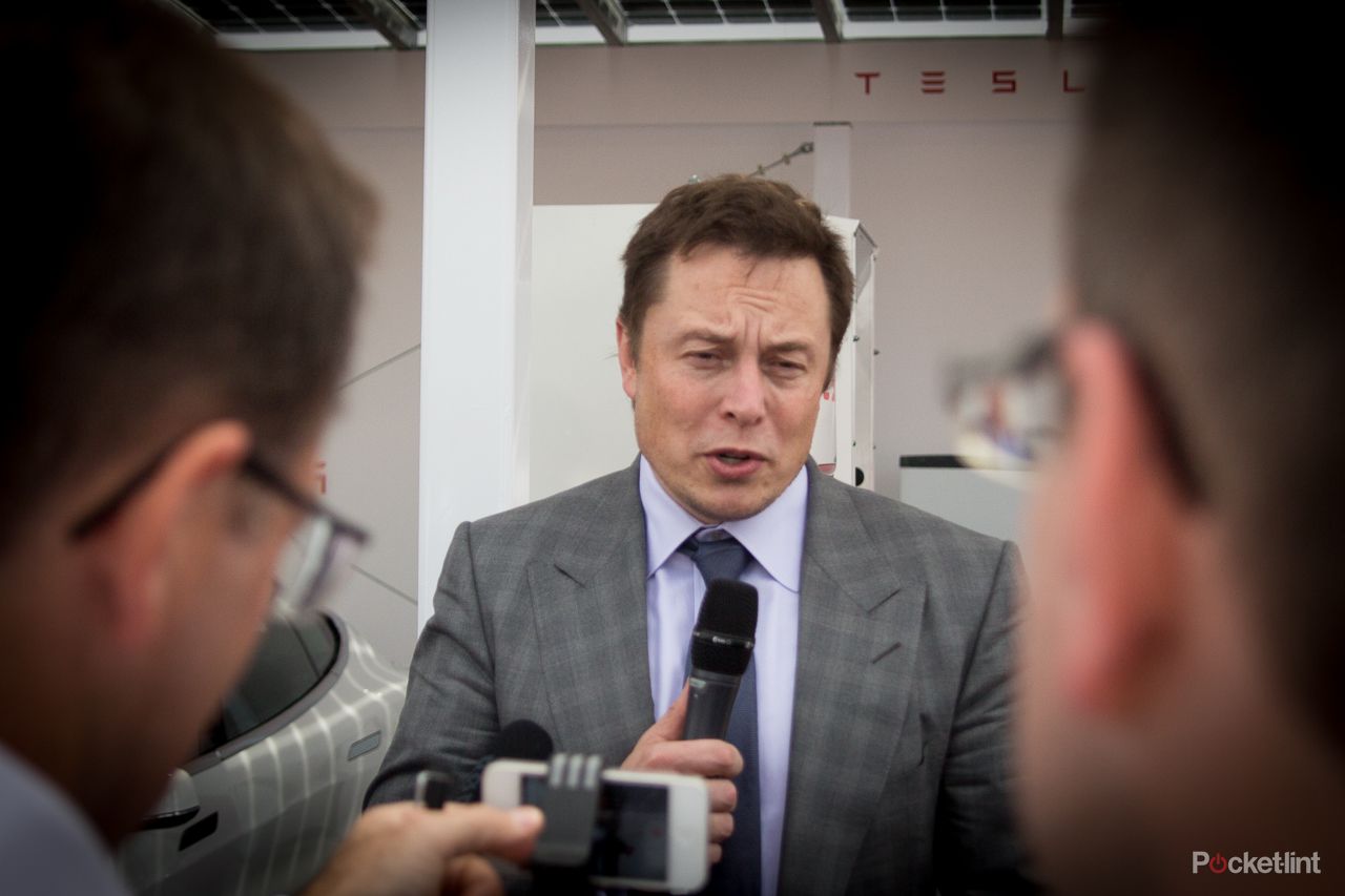 Elon Musk holding a microphone speaking with reporters