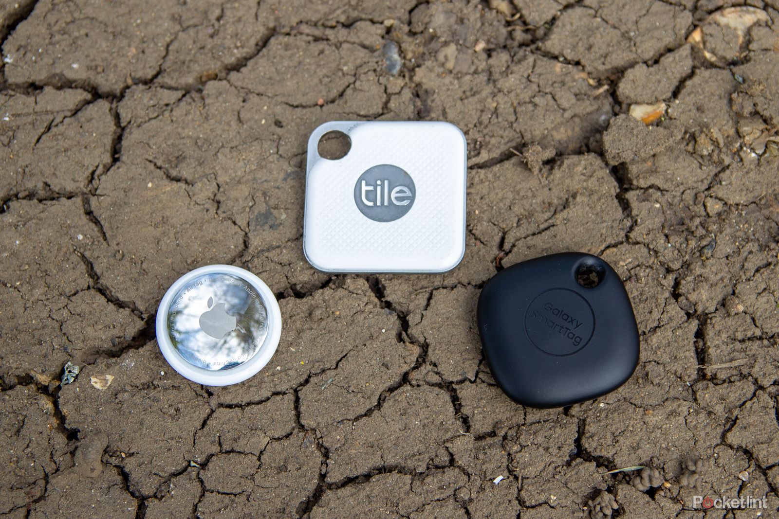 Apple AirTag and two Tile trackers on a cracked mud floor