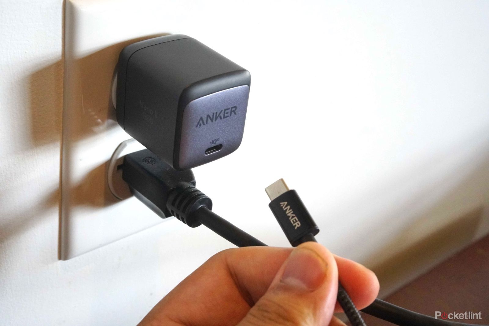 Anker Nano II 45W USB-C charger block plugged into wall with USC C charging wire held in hand next to it.