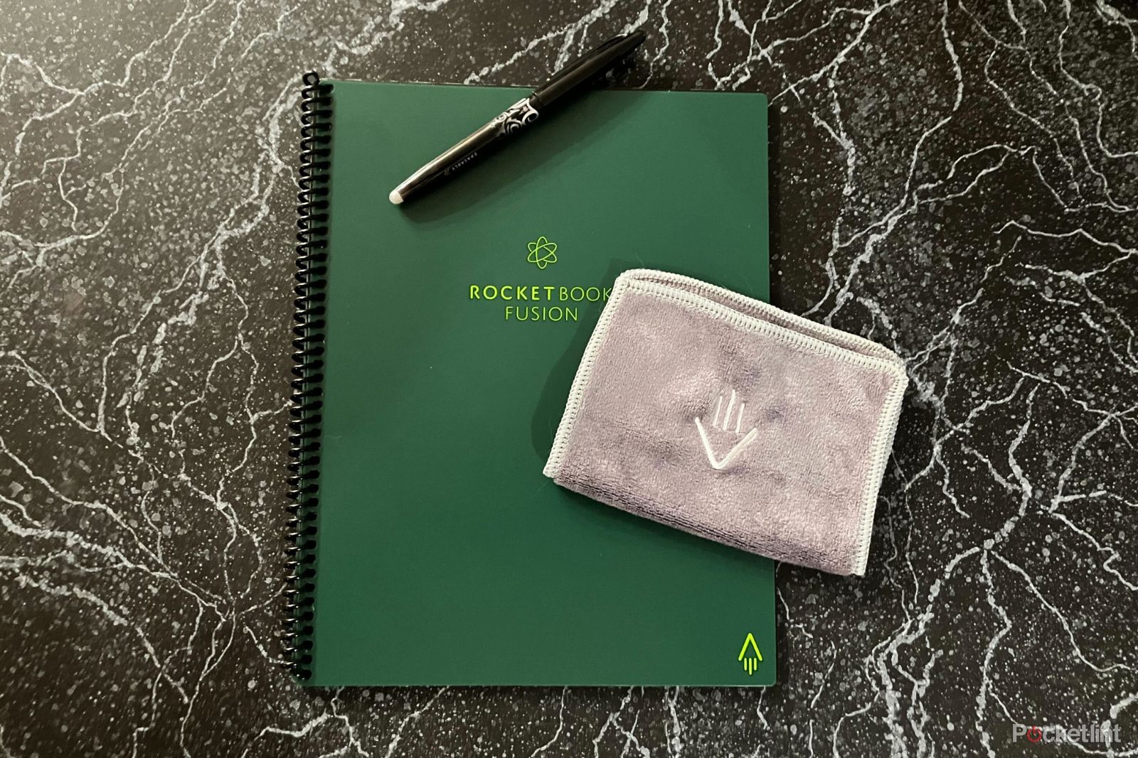Green Rocketbook Fusion Notebook on black countertop with microfiber cloth and pen on top