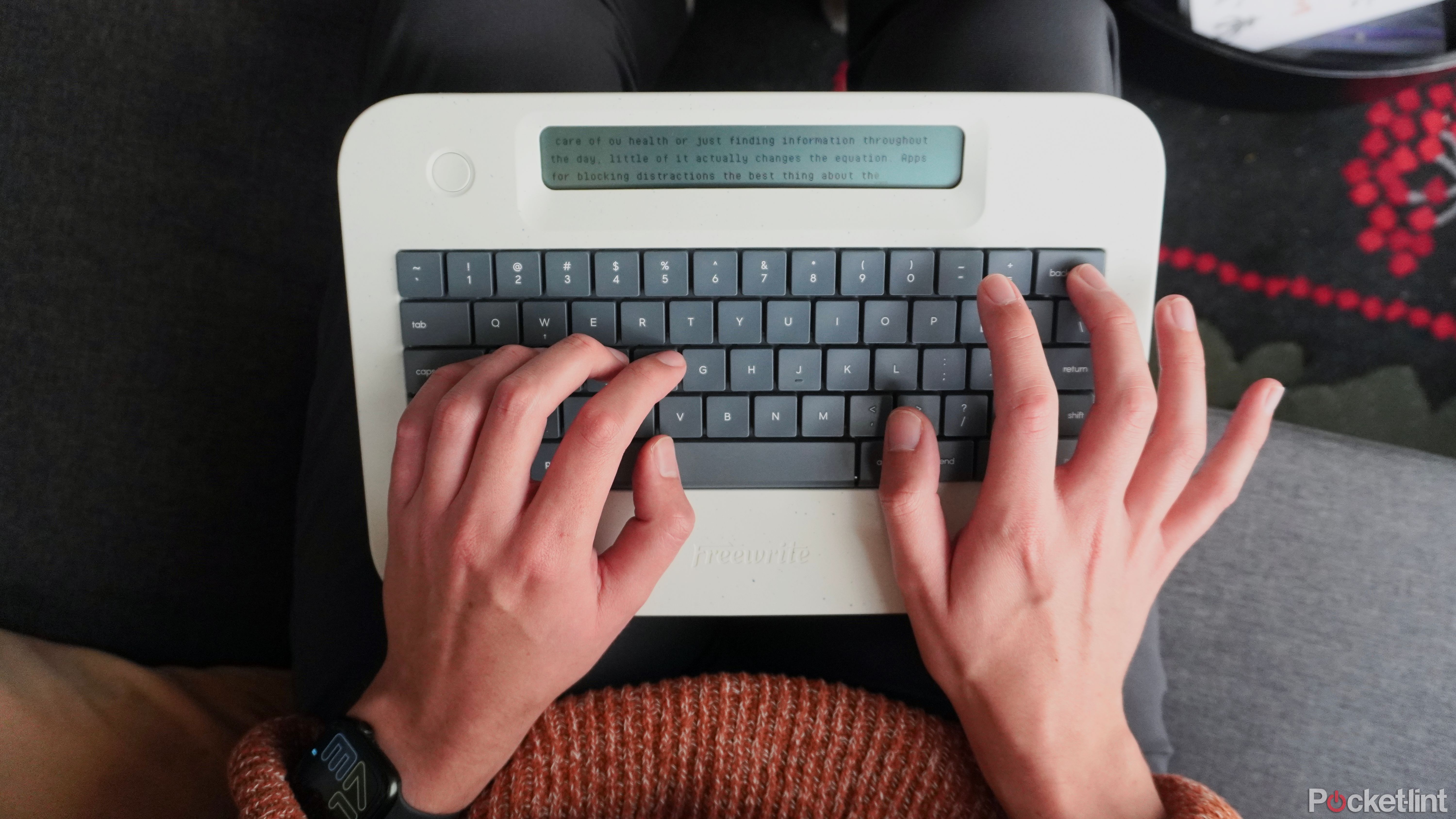Two hands typing on a Freewrite Alpha on a lap.