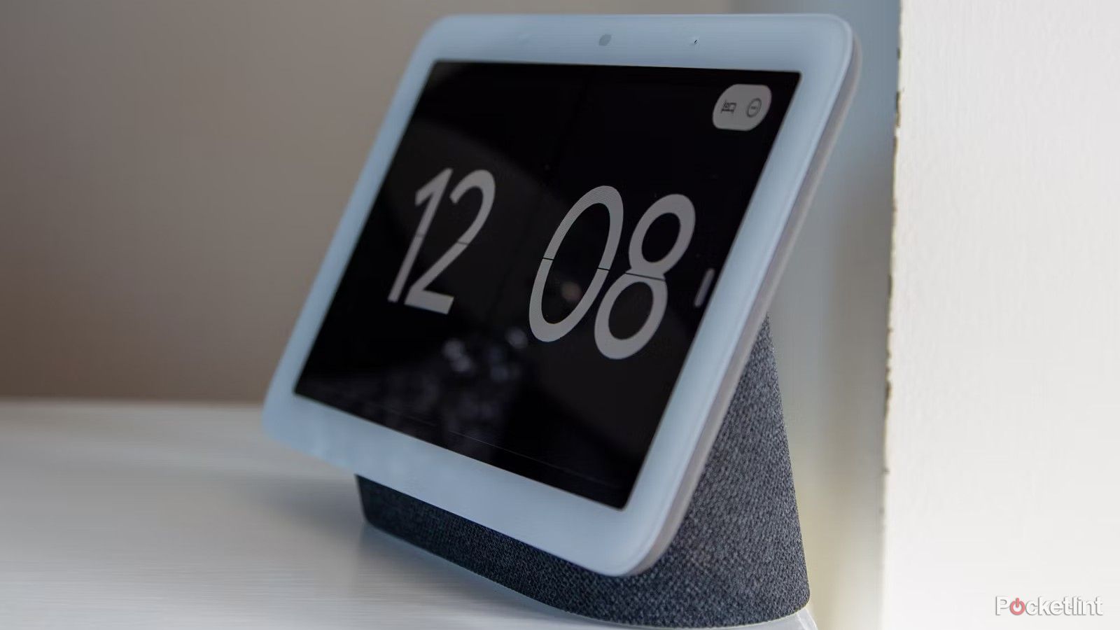 A charcoal Google Nest Hub sits next to the wall