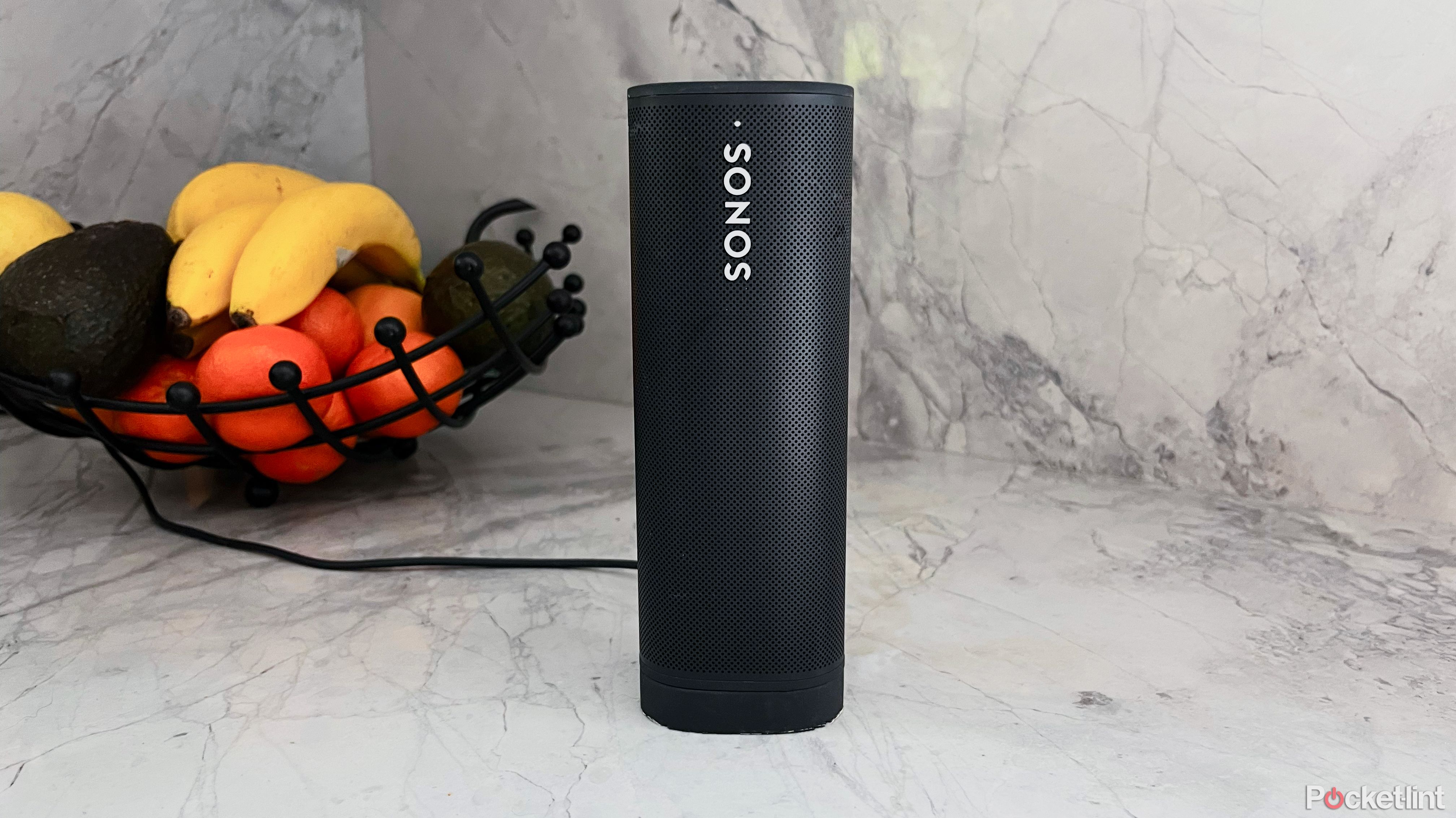 A Sonos Roam sitting on it's charger on a countertop.