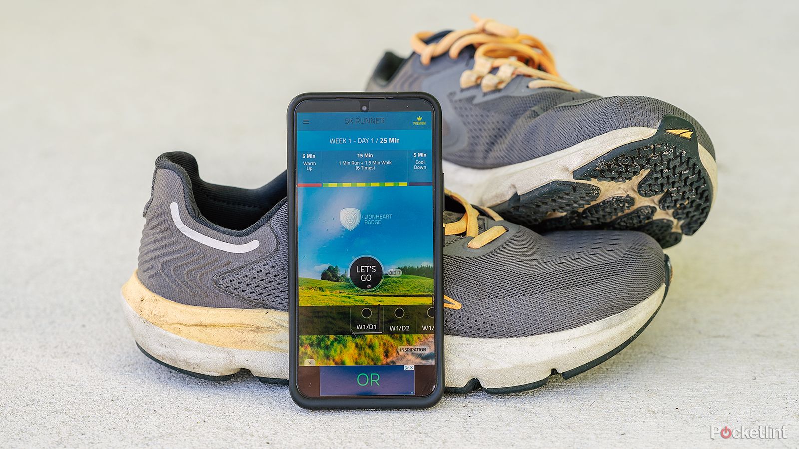 A phone displays the 5K Runner app while leaning against running shoes. 