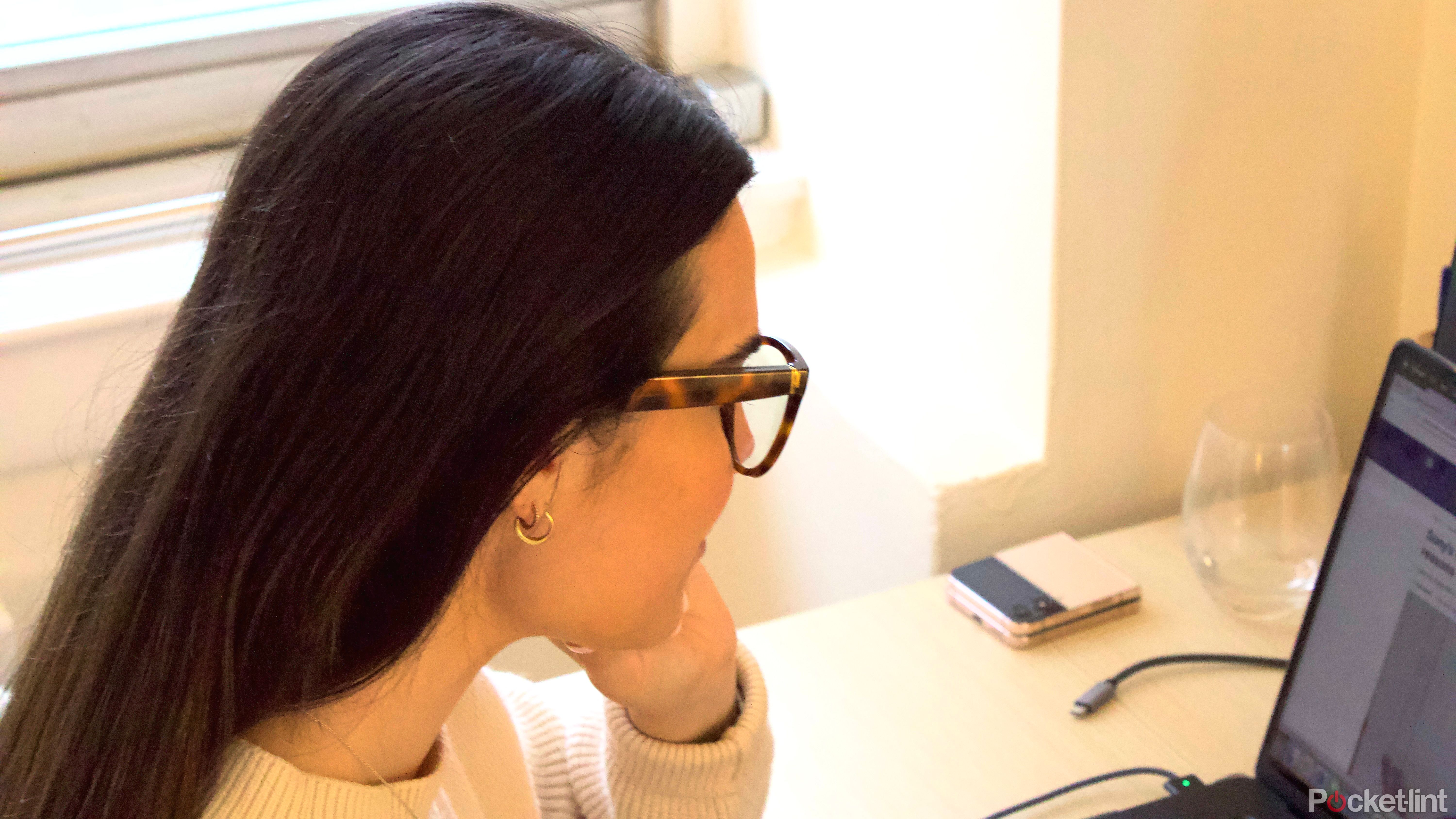Νεαρή γυναίκα με σκούρα μαλλιά που εργάζεται και φοράει καρέ Amazon Echo 3ης γενιάς