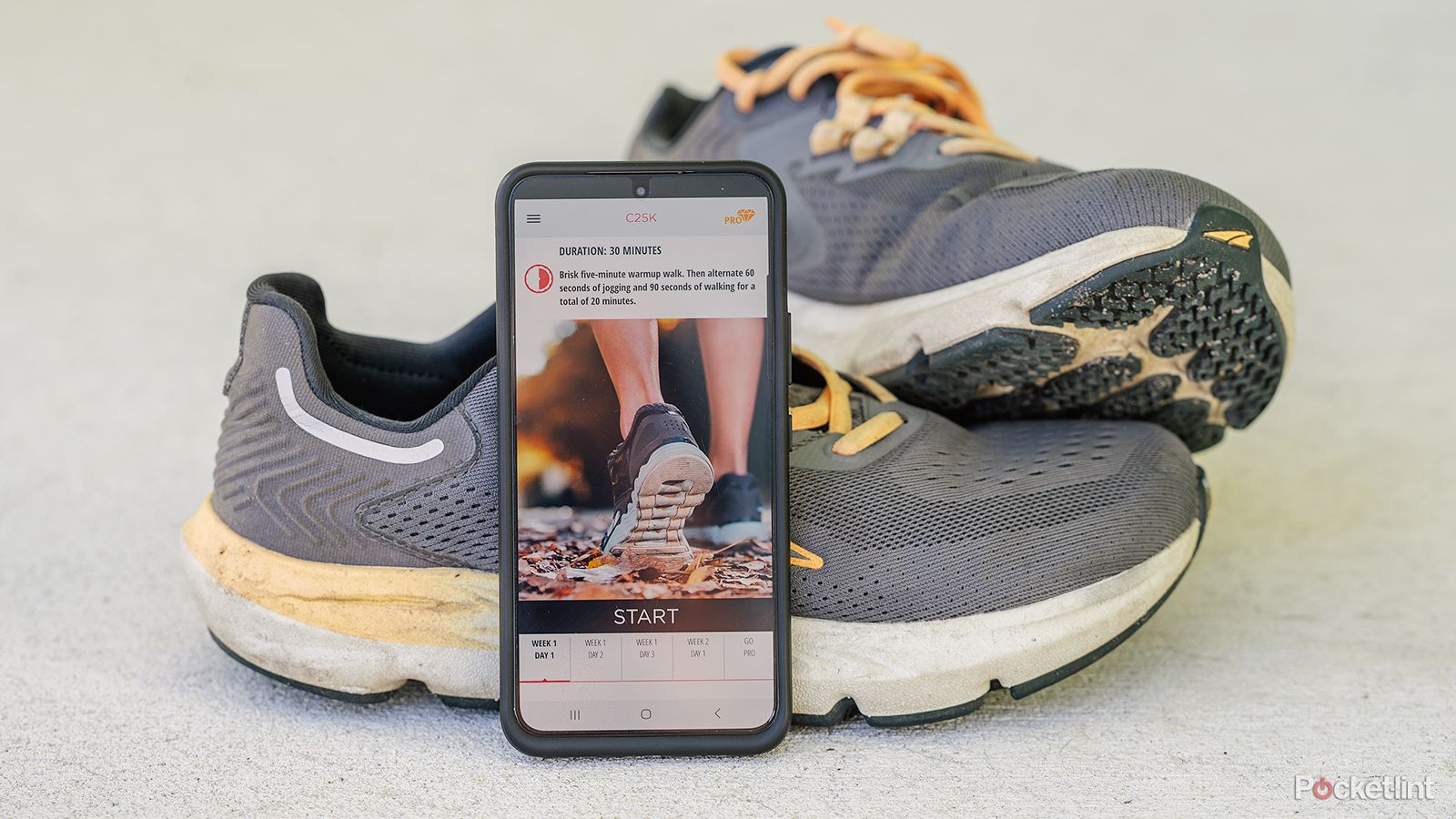 A phone displays the C25K app while leaning against running shoes. 
