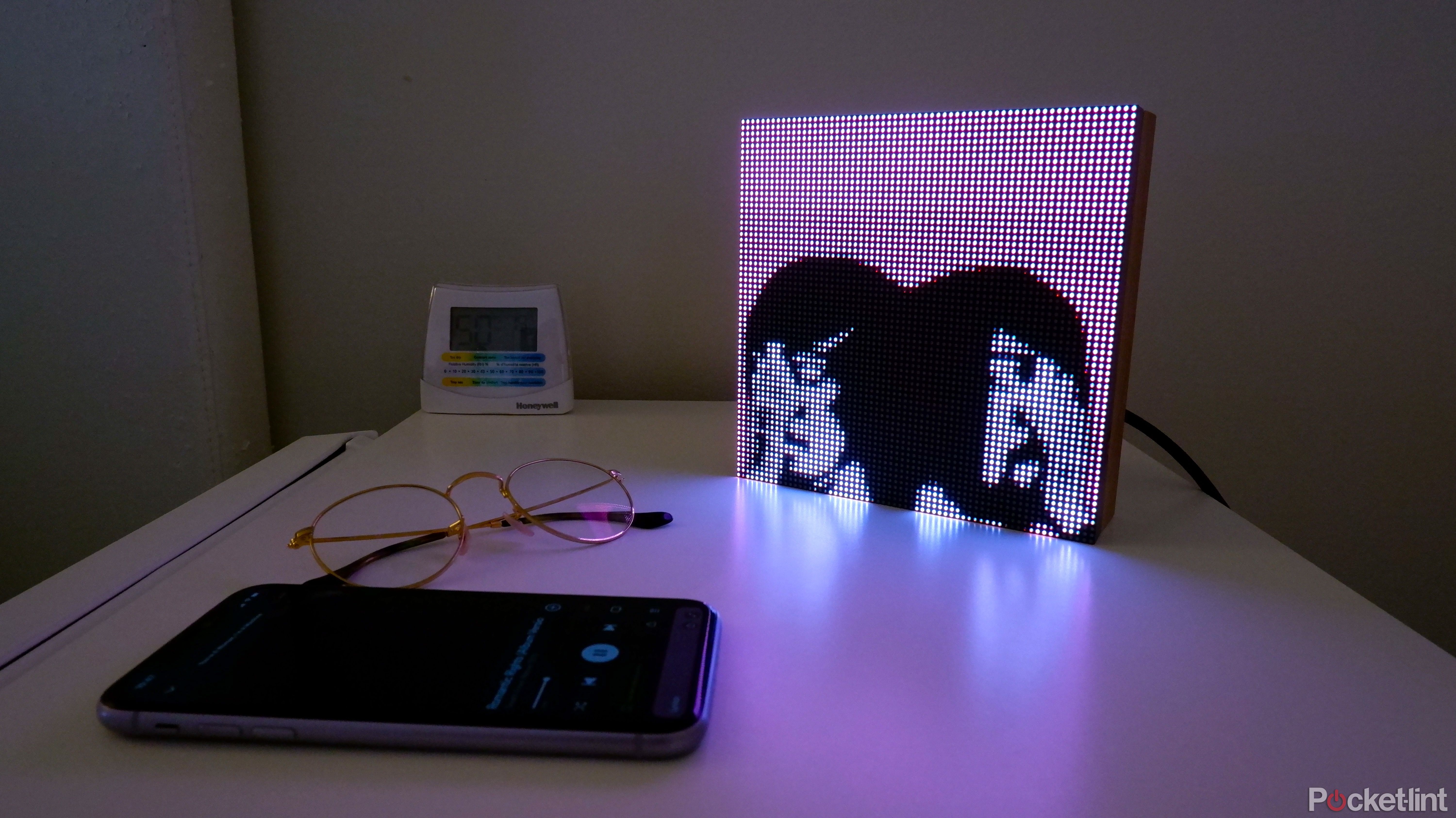 A Tuneshine on a bed side table displaying album art for Death from Above 1979, next to an iPhone and a pair of glasses.