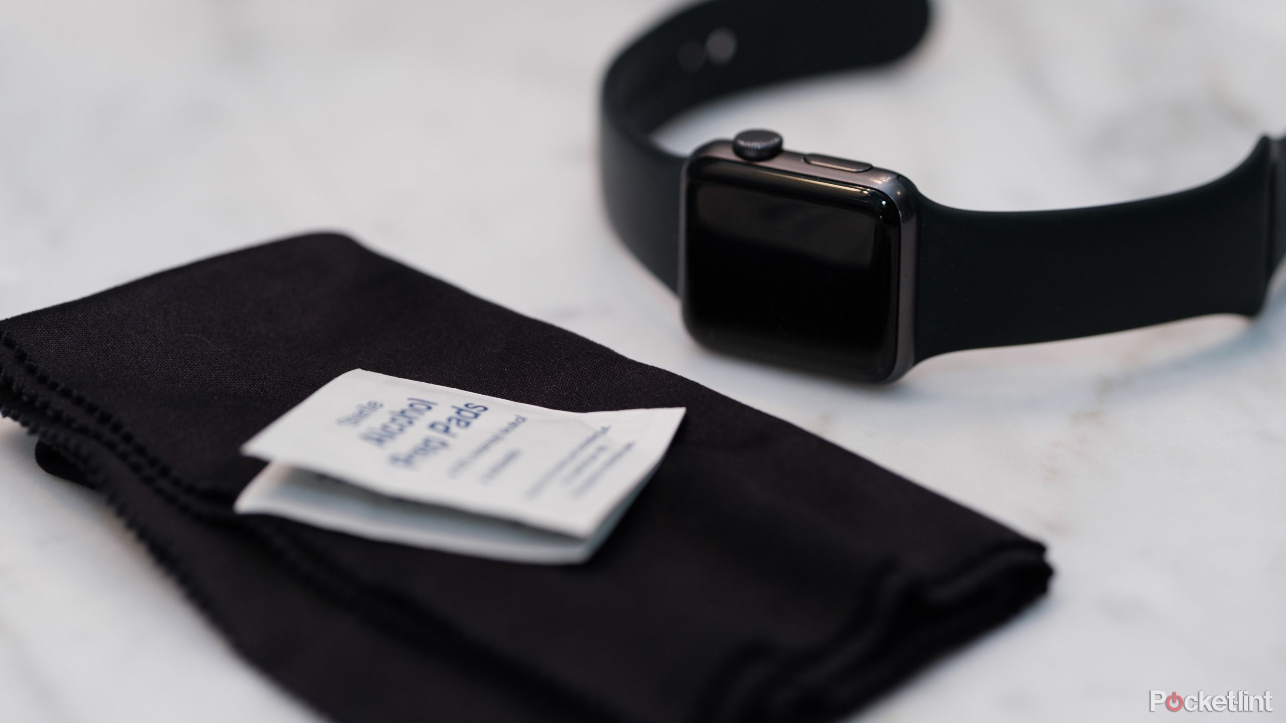 A photograph of a smartwatch with a microfiber cloth and alcohol wipe