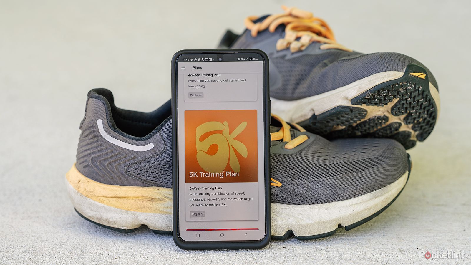 A phone displays the Nike Run Club app while leaning against running shoes. 