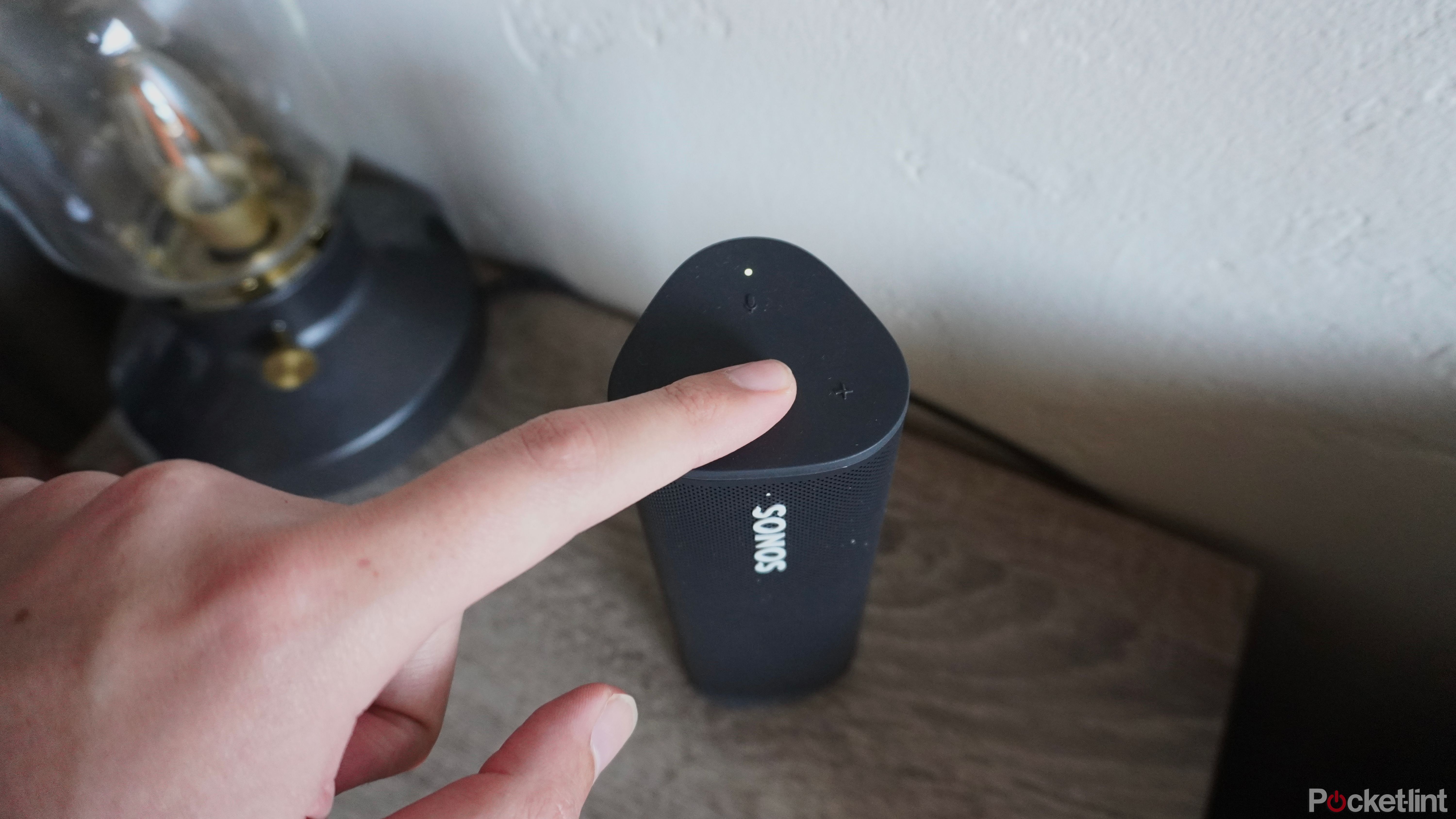 Pressing the Play/Pause button on a Sonos Roam speaker.