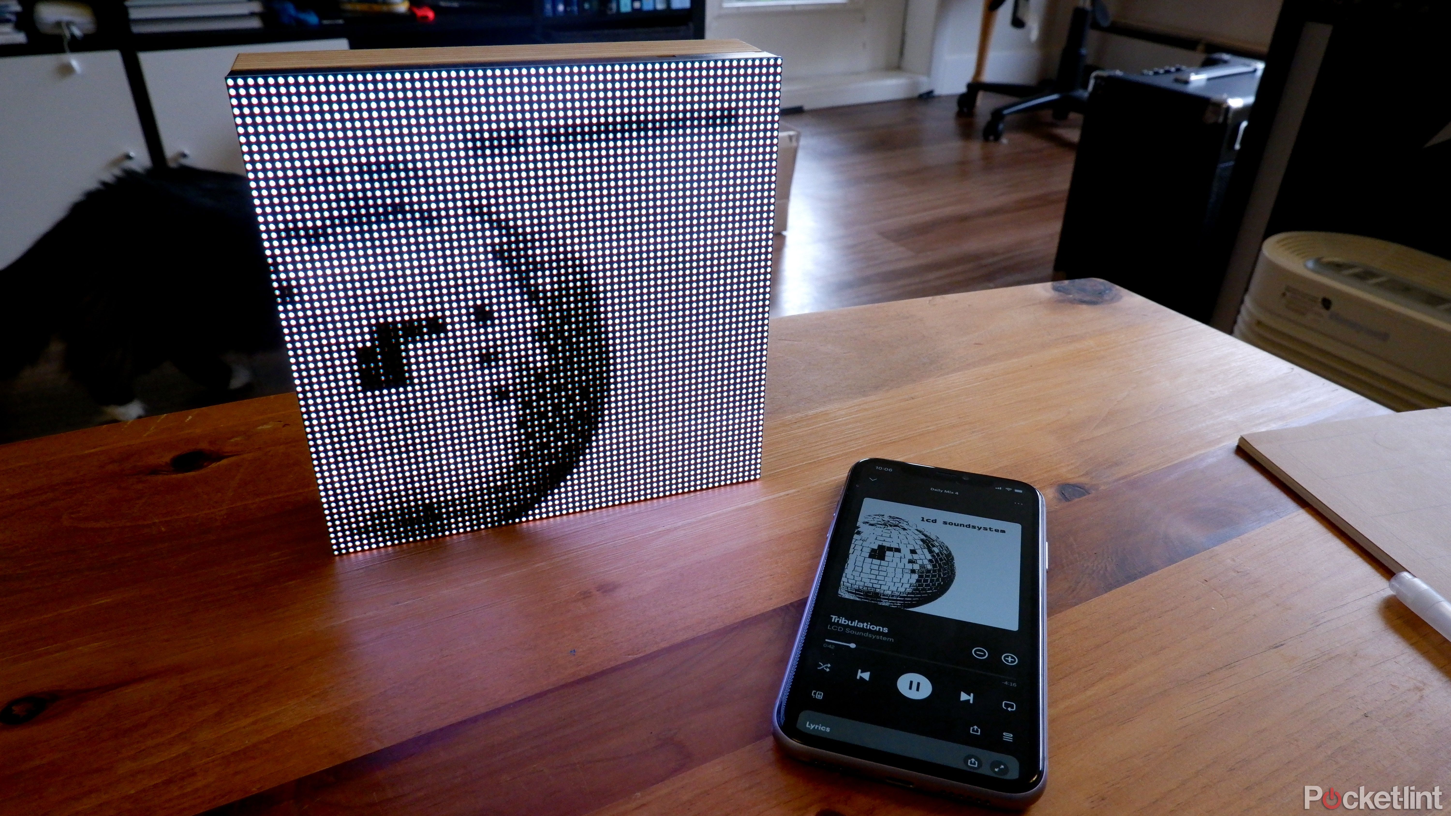 A Tuneshine on a coffee table displaying LCD soundsystem album art, next to an iPhone with Spotify open.