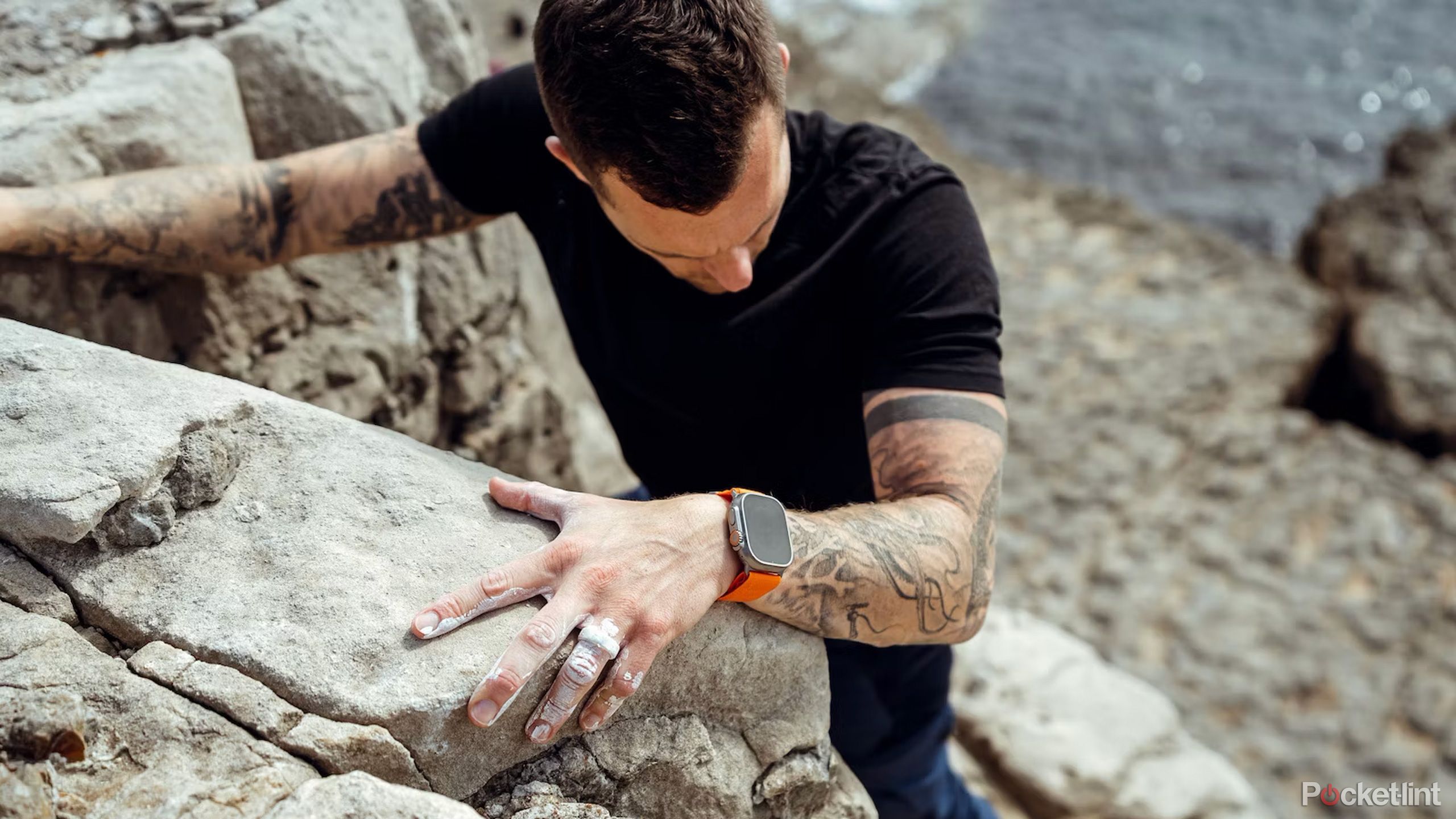 A tattooed man climbs a cliff face with an Apple Watch Ultra 2 on his wrist