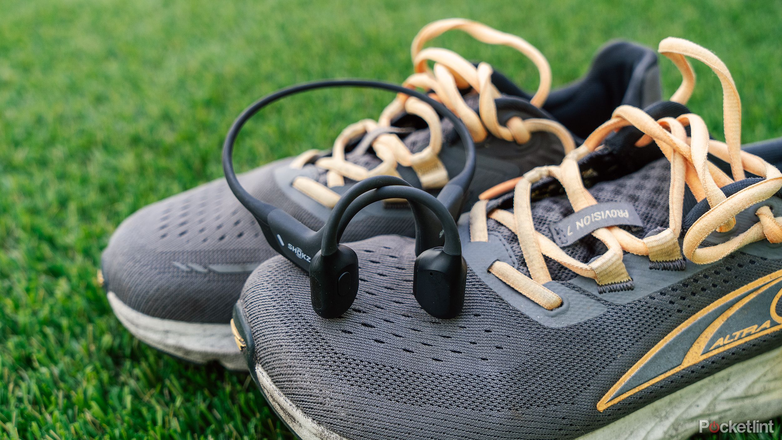 A pair of Shokz bone conduction headphones sits on a pair of gray running shoes. 