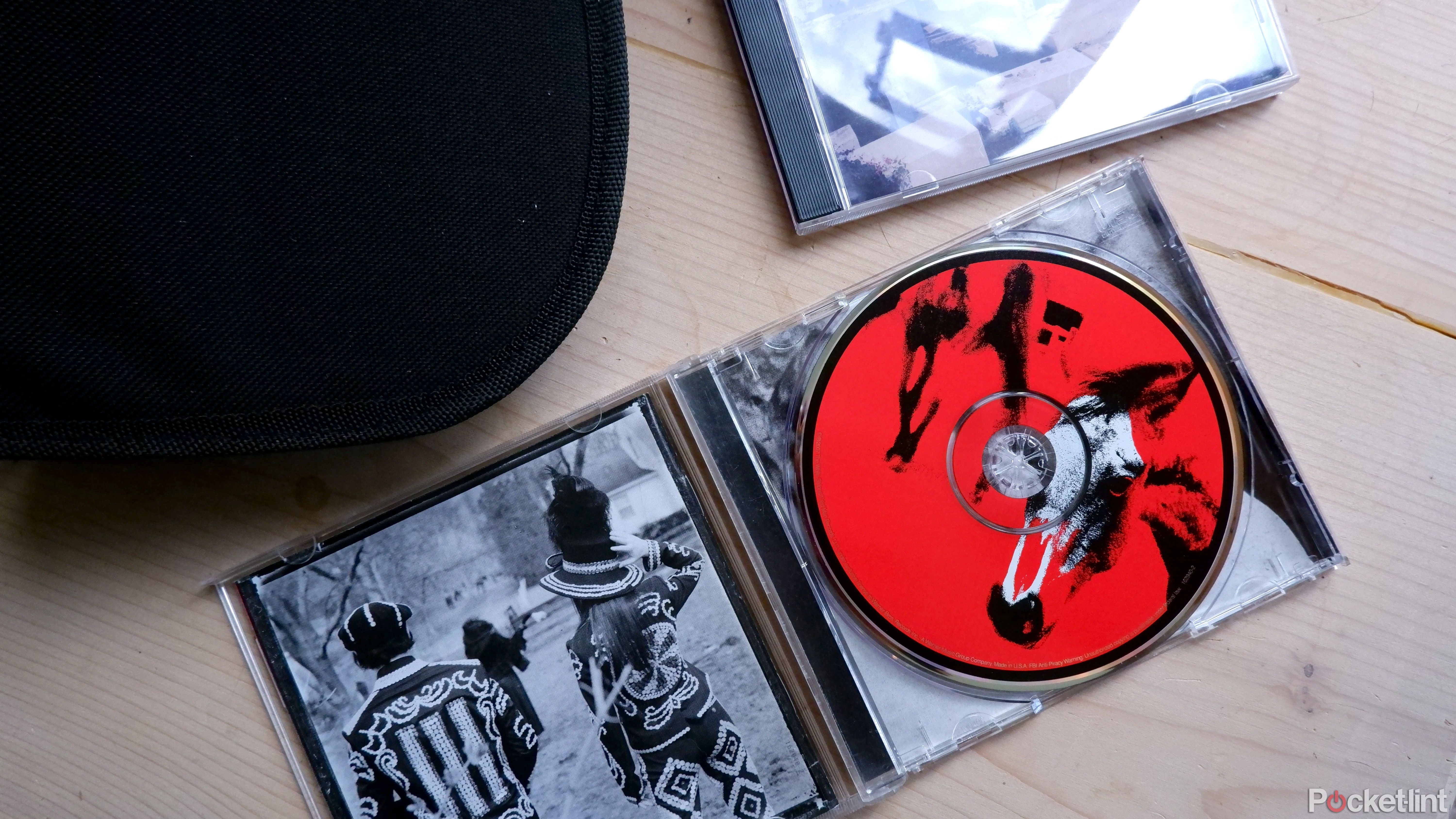 An open CD case, a travel case, and a closed CD case laid out on a wooden surface